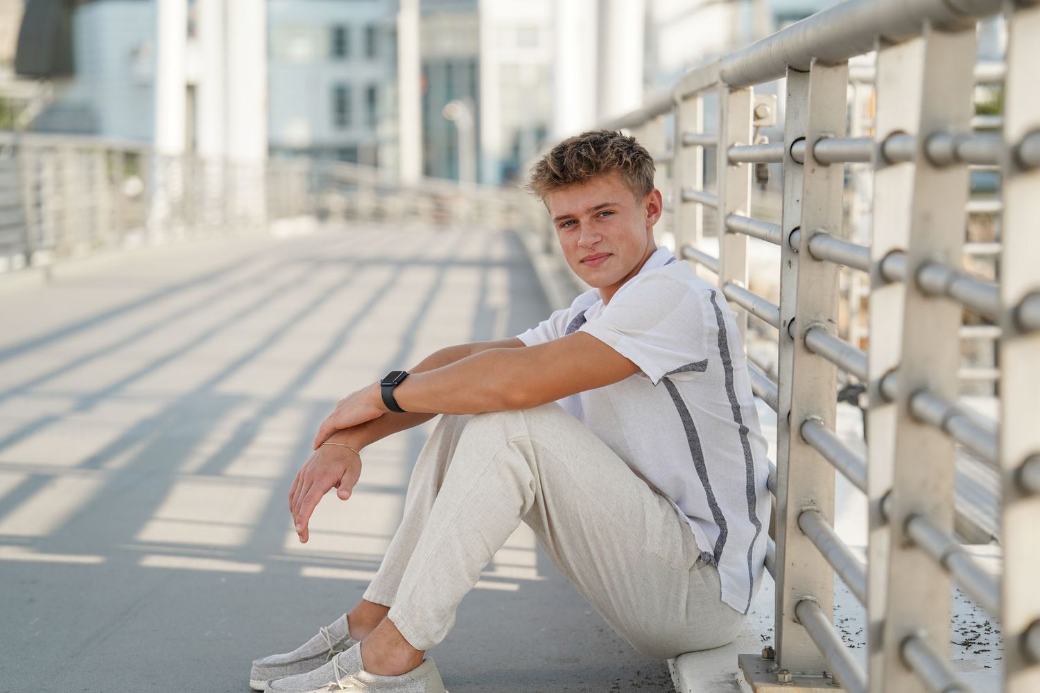 A person in casual attire poses against metal railings on a bright minimalist urban rooftop or balcony area.