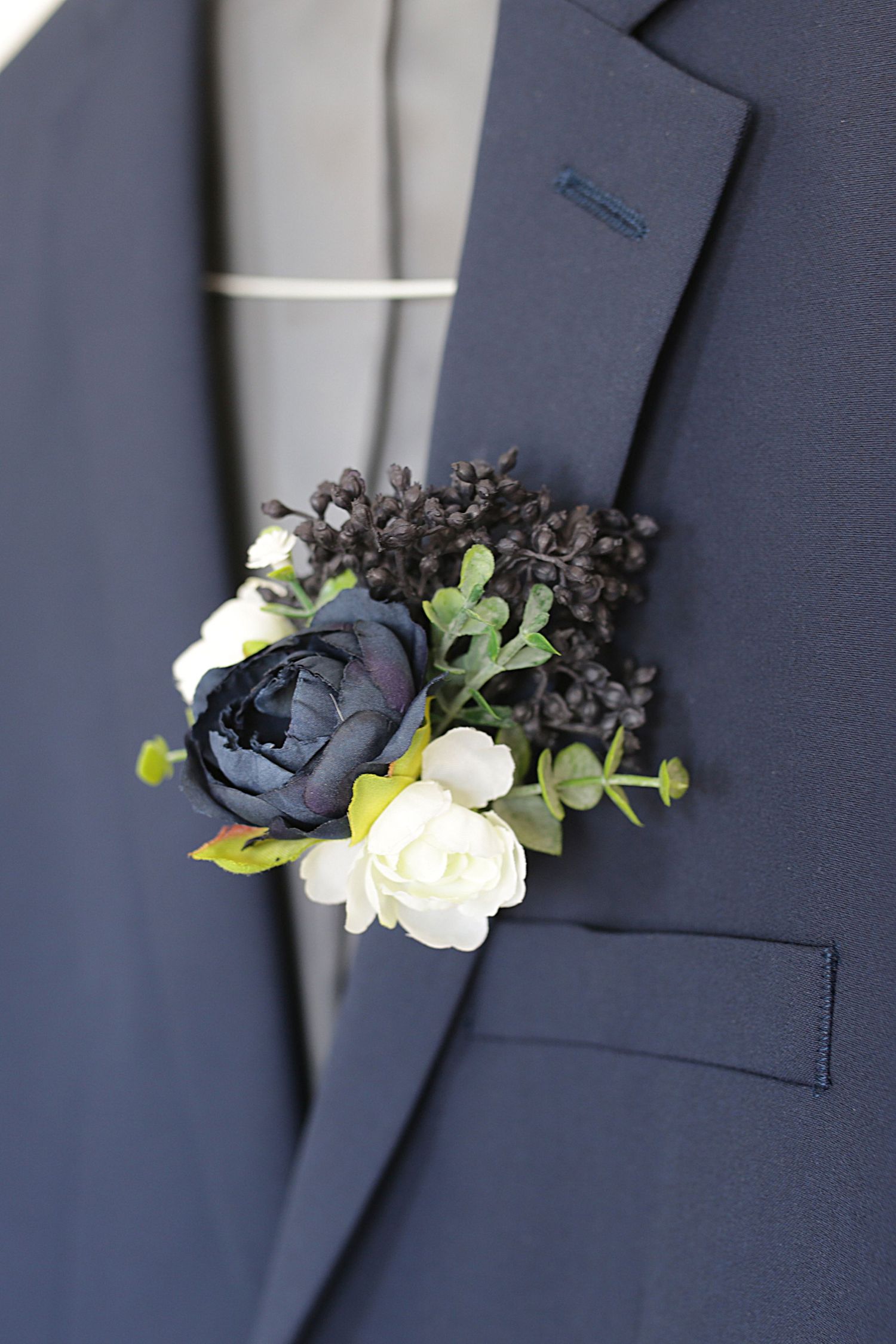 A navy blue boutonniere featuring black and white flowers with delicate greenery on a dark suit lapel.