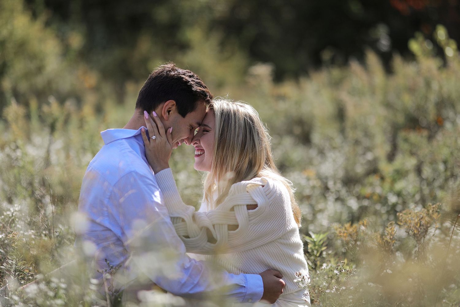 A romantic couple shares an intimate moment while sitting in a sunlit meadow with wildflowers.