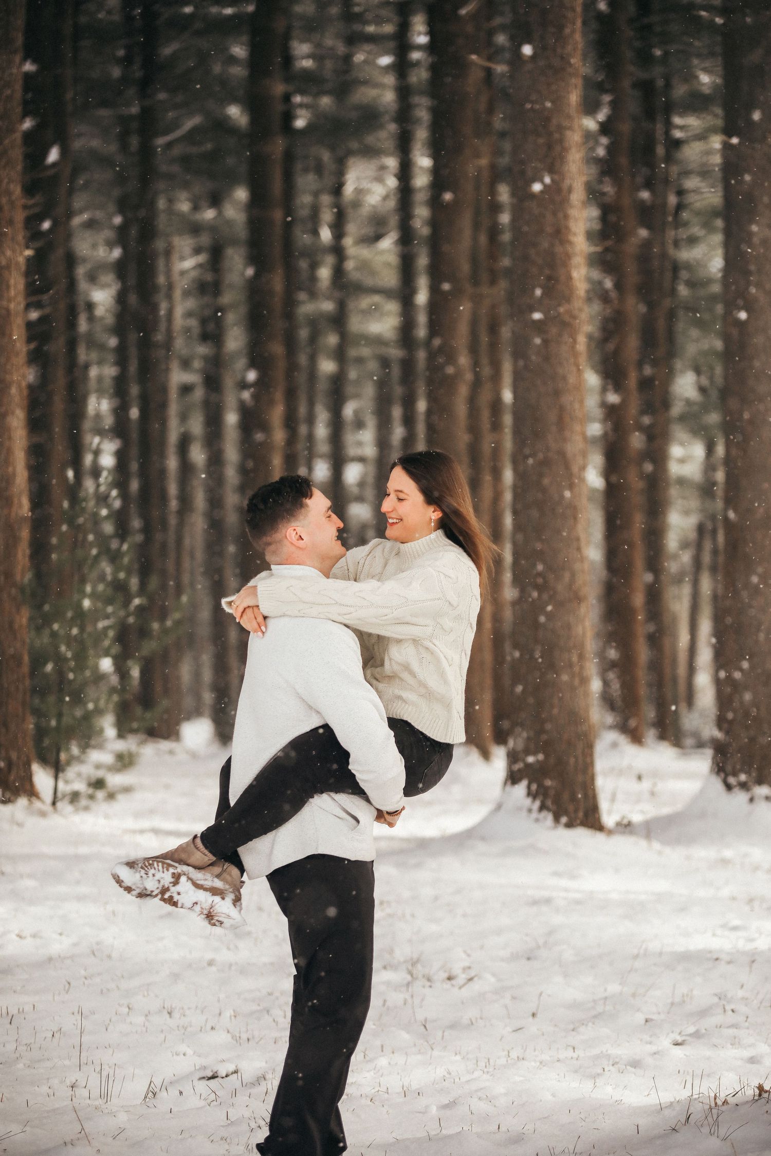 A couple in formal attire shares a romantic moment in a snowy winter forest setting.