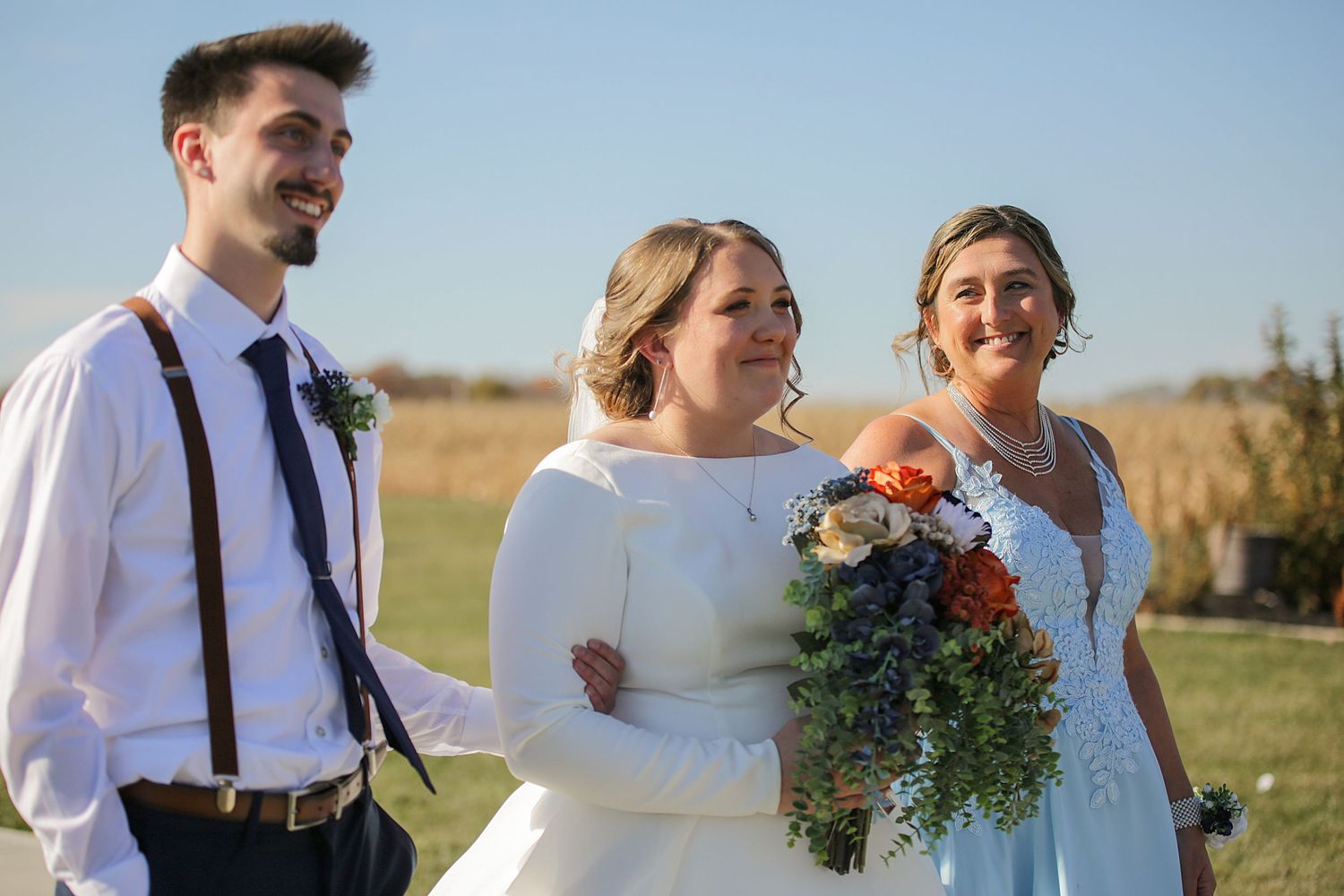 Wedding party poses on hillside during sunset ceremony with flowing veil and wildflower bouquets.