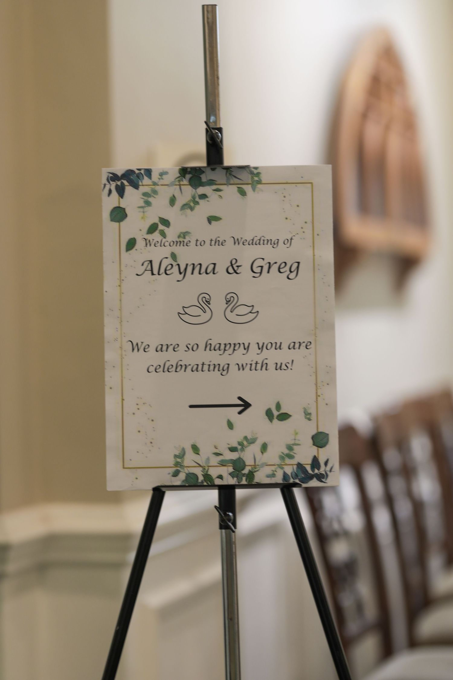 Wedding welcome sign on black easel stand features floral design and text welcoming guests to Aleyna and Greg's celebration.