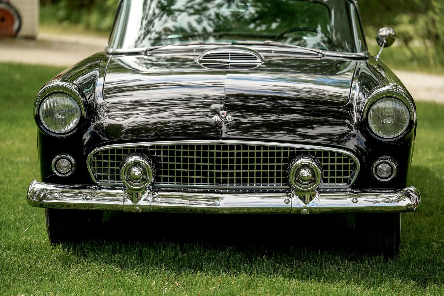 Close-up view of a classic black Ford Thunderbird's front grille and headlights parked on grass.
