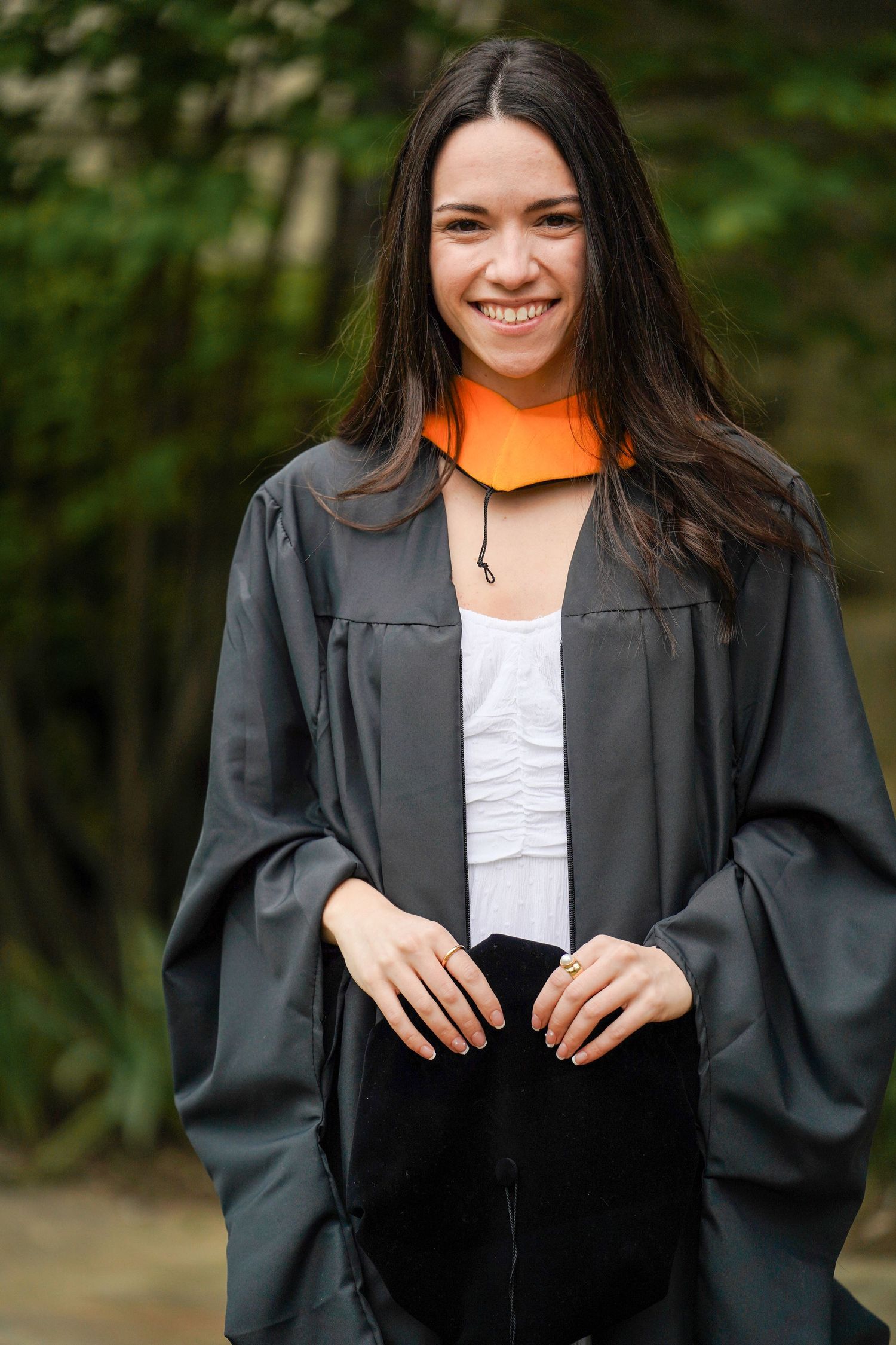 Graduate in black cap and gown poses outdoors with joyful expressions in a series of professional portraits.
