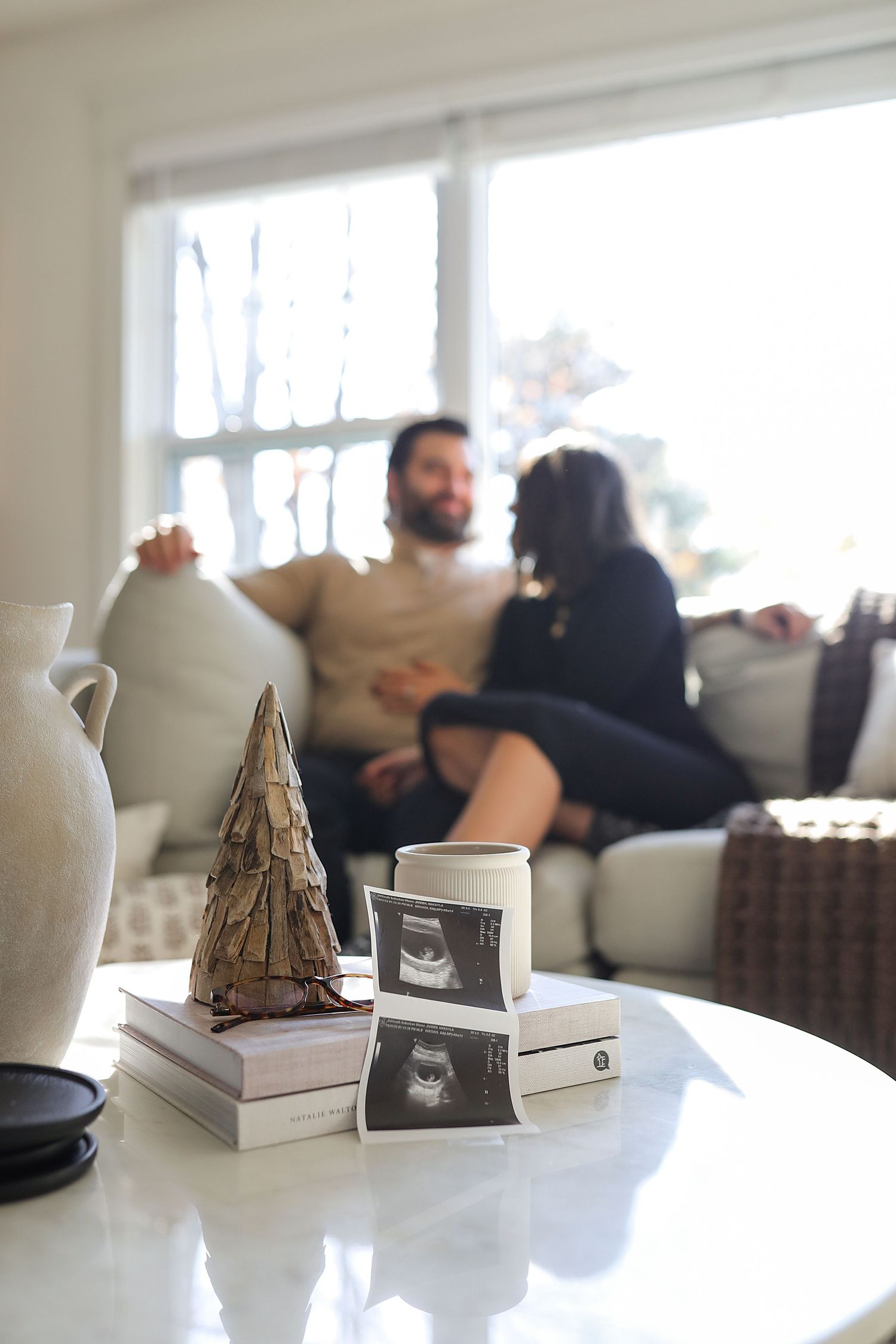 Ultrasound photos and decorative items on coffee table with couple relaxing on couch in background.