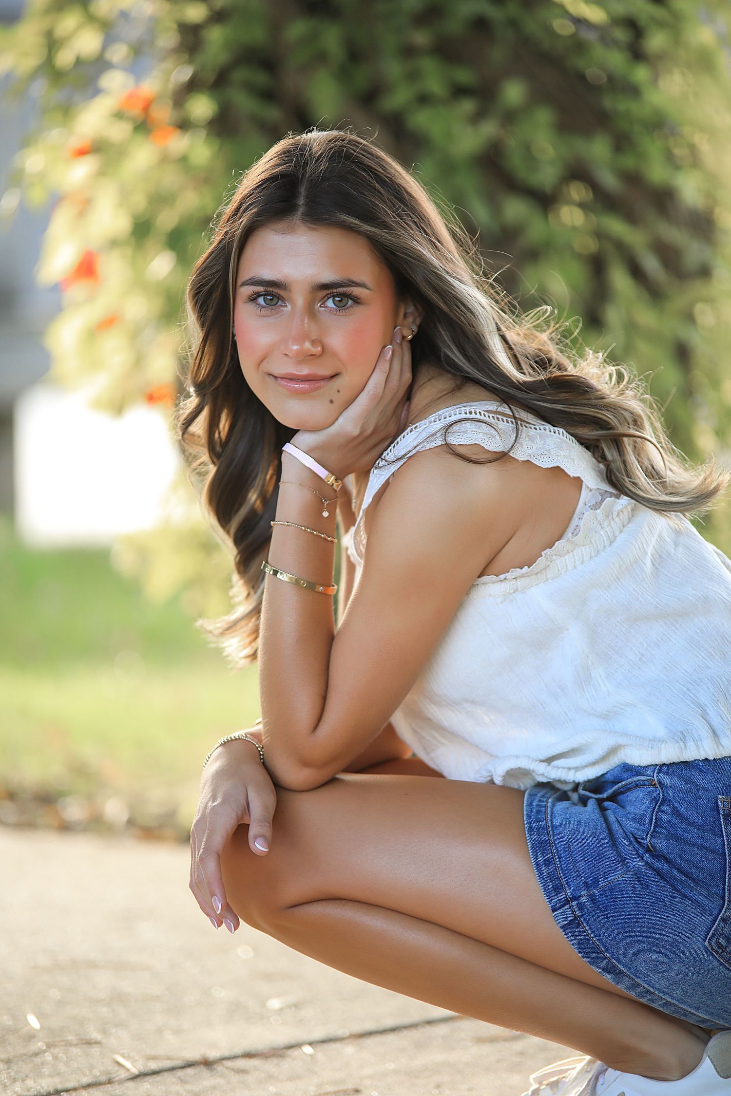 A warm outdoor photoshoot captures a person in white top and denim shorts posing on the ground in natural lighting.