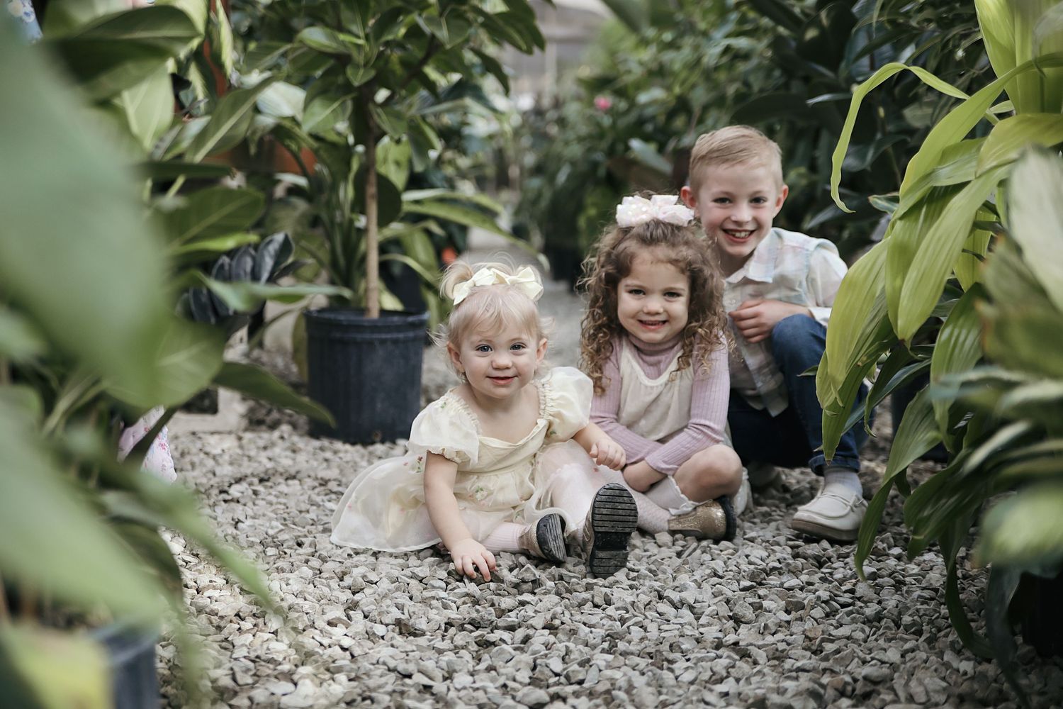 Young family lying on gravel pathway surrounded by lush green plants in an outdoor garden setting.