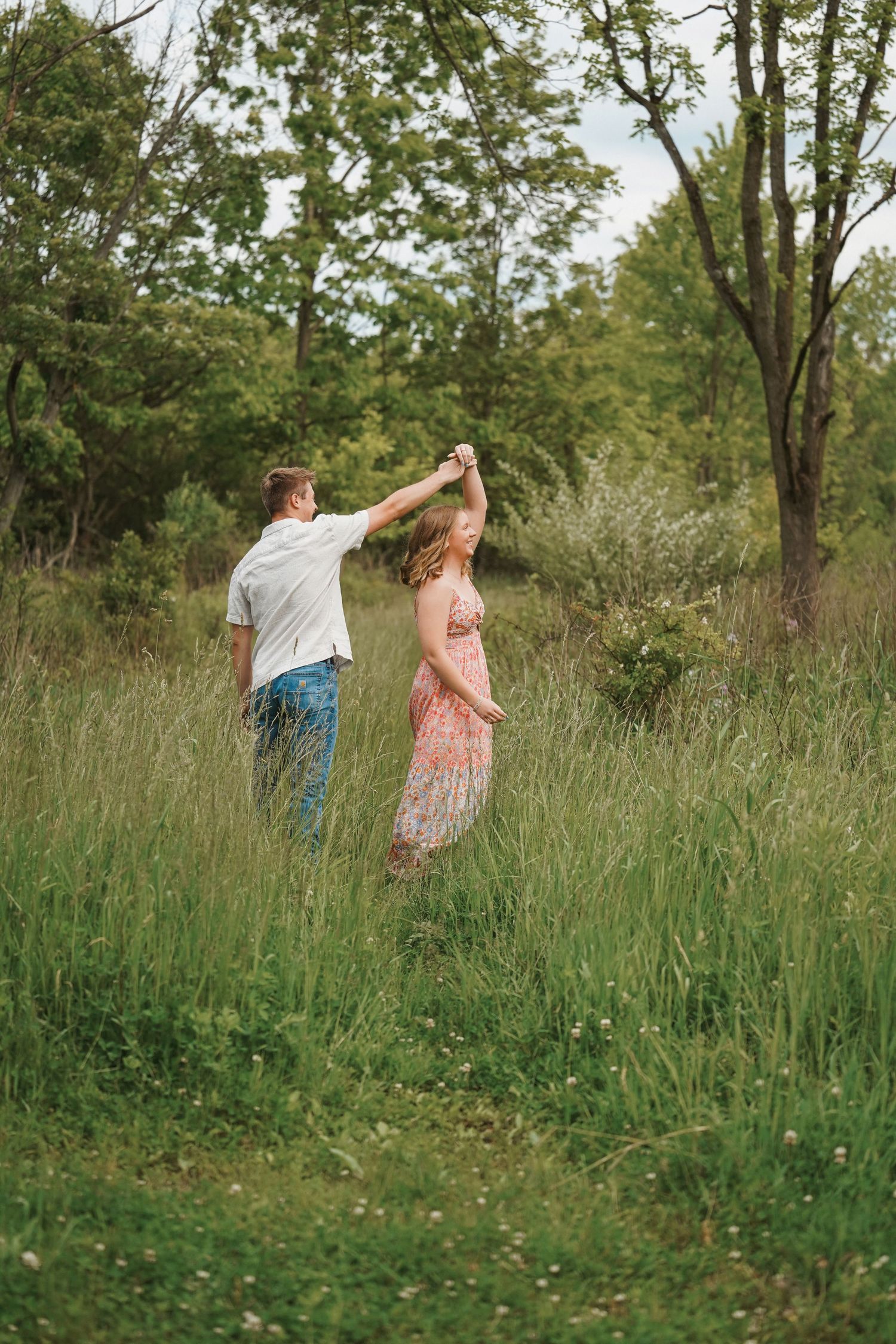 A couple dancing together in a meadow surrounded by tall grass and trees on a sunny summer day.