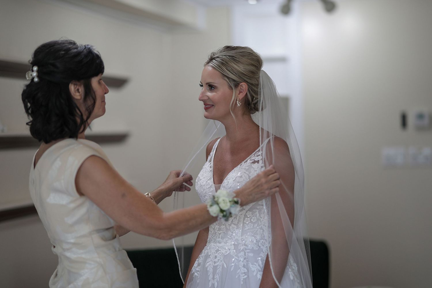 A touching moment during wedding preparations shows final dress adjustments in a brightly lit room.
