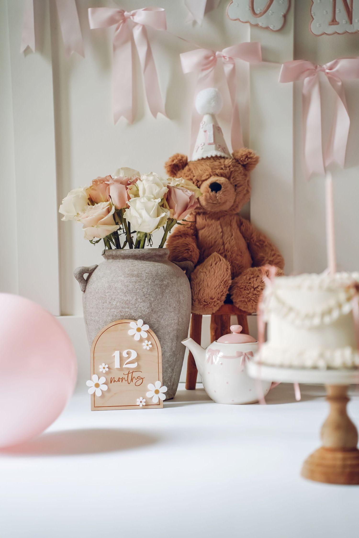 Pink and white baby shower decorations with teddy bears, bows, and cake stands create a delicate nursery theme display.