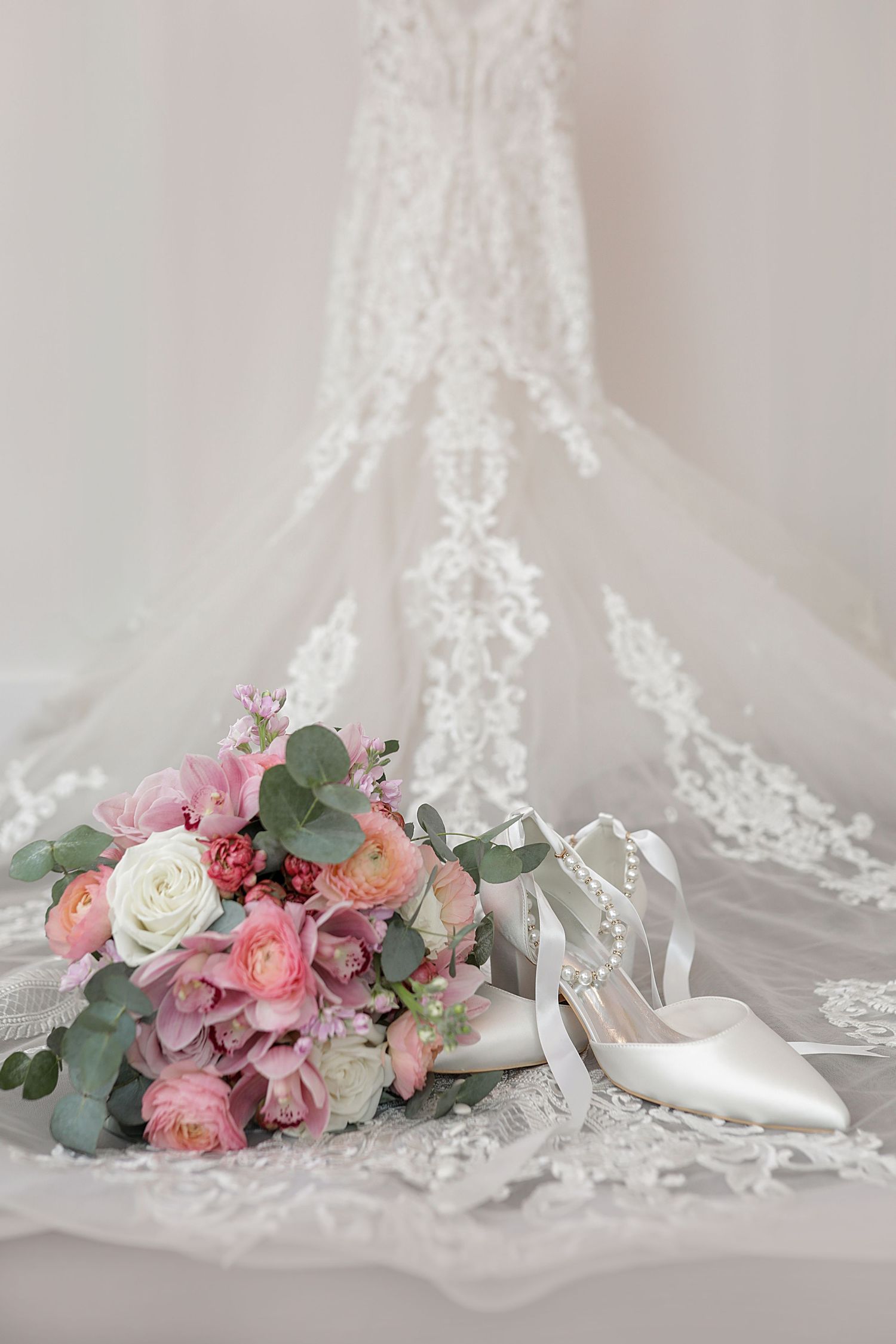 Elegant bridal bouquet with pink roses and eucalyptus leaves alongside white heels and lace veil. Cleveland wedding photographer.
