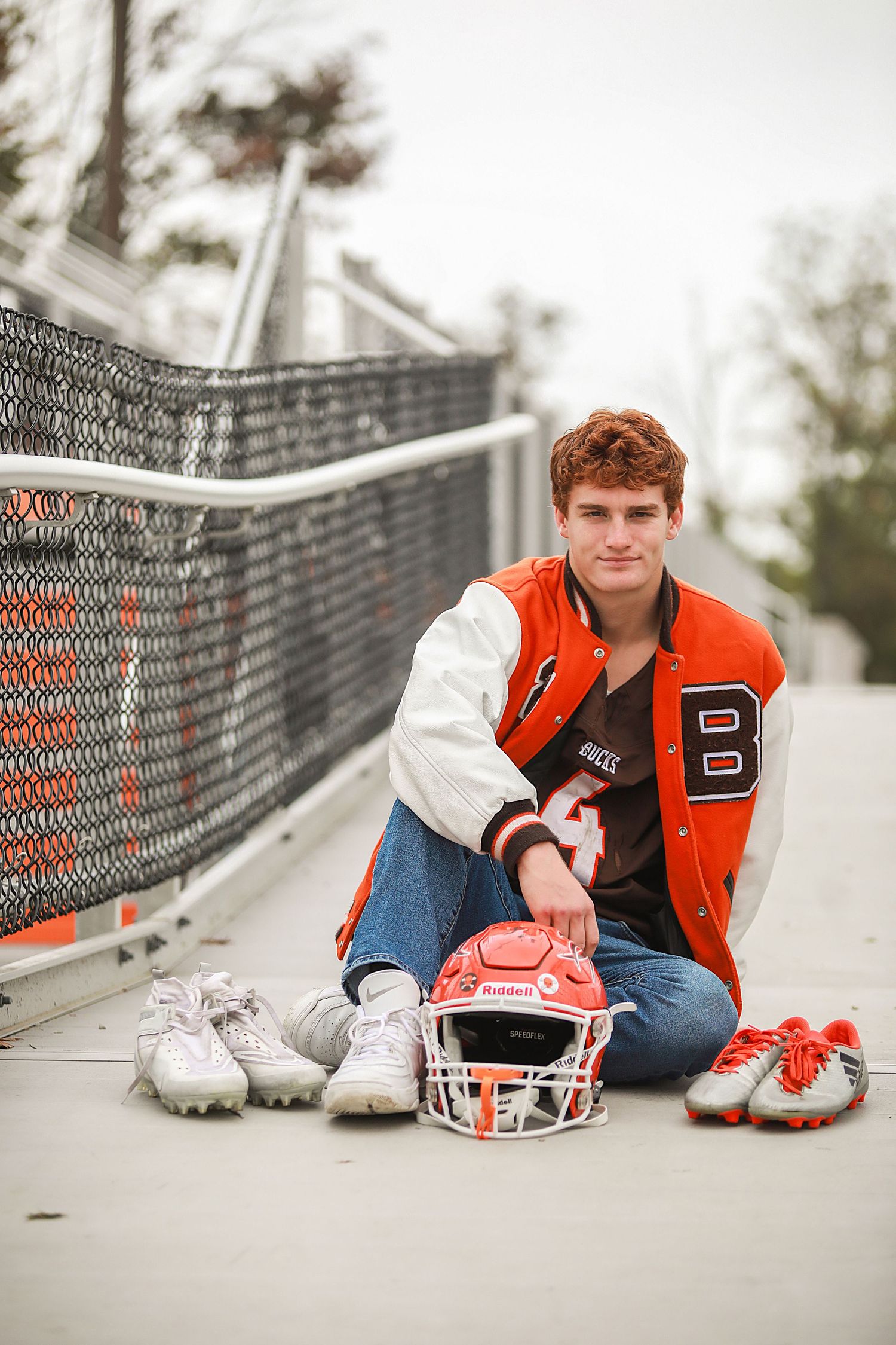 Sports themed senior portrait with football gear and orange letterman jacket on bridge. Senior Photography in Brunswick, Ohio