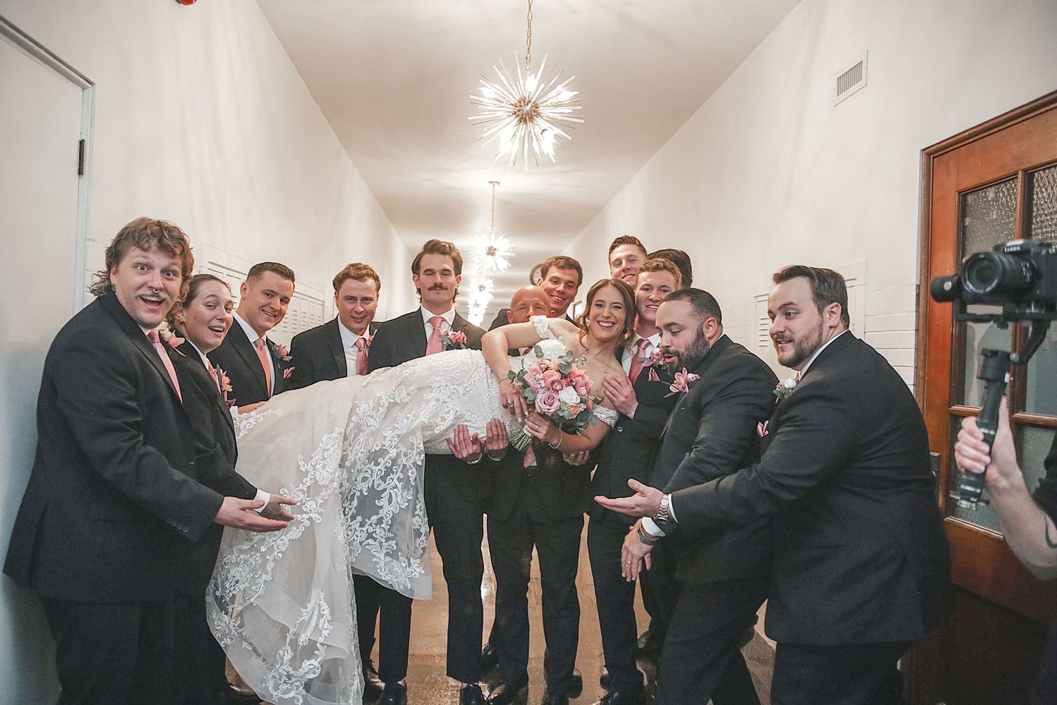 A group of formally dressed guests in black suits and ties gather in a hallway during a celebration event.