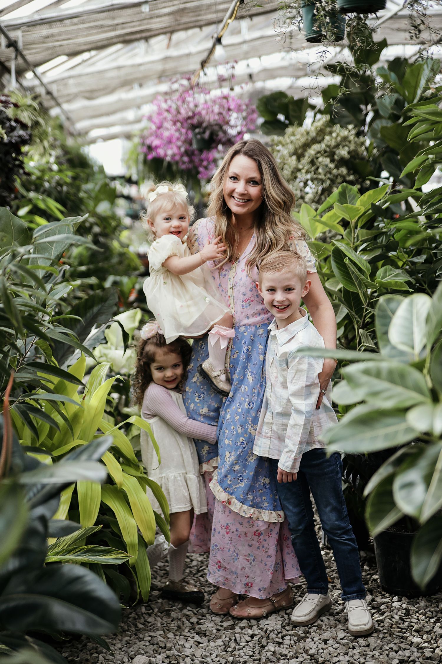 A family poses together in a lush greenhouse filled with tropical plants and hanging pink flowers.