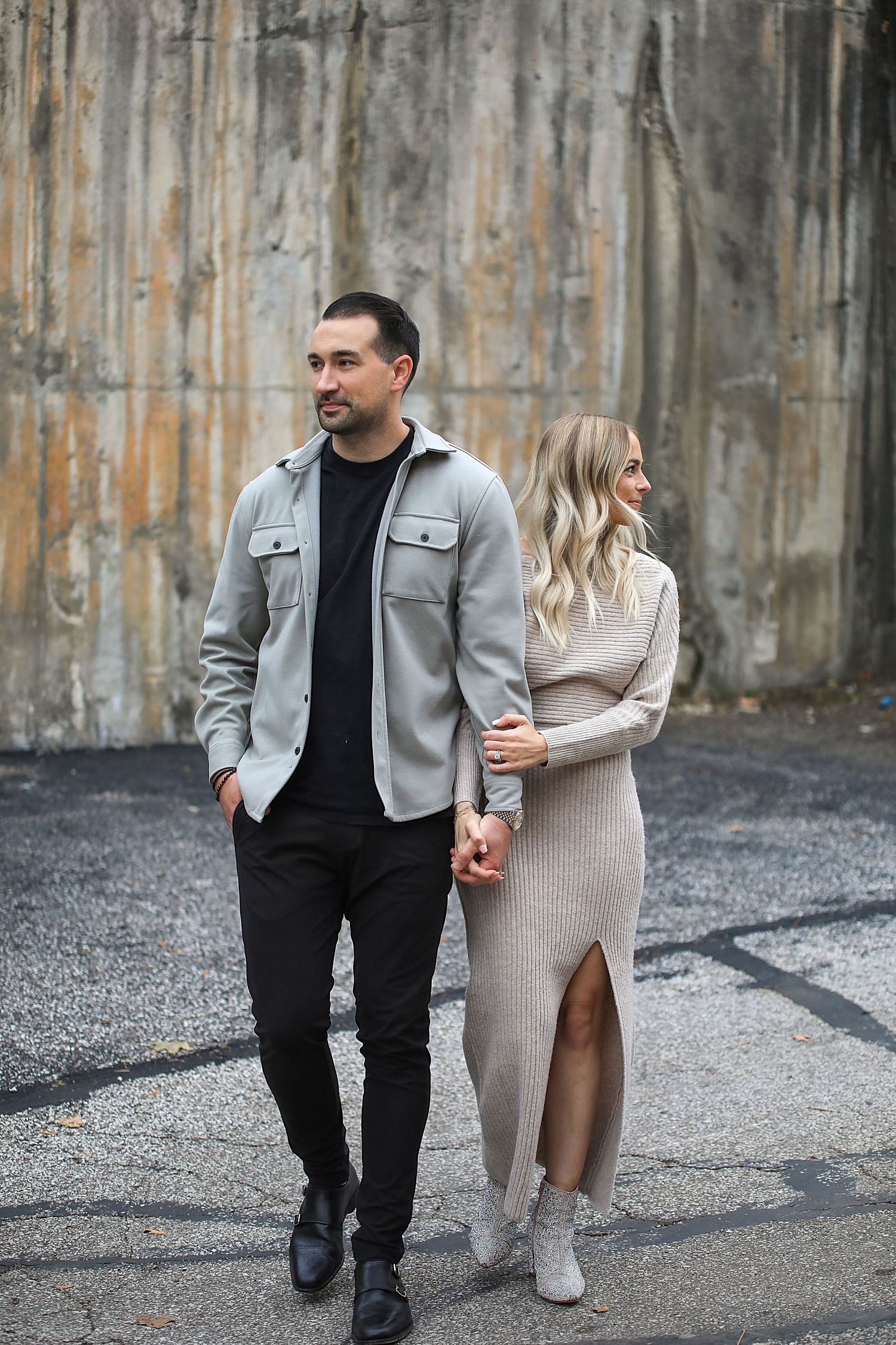 Stylish couple poses against industrial concrete wall in casual chic outfits. Engagement photographer in Chagrin Falls, Ohio