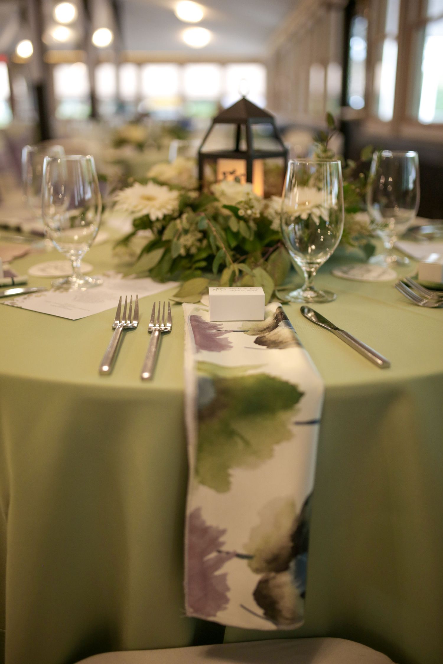 Elegant wedding reception table settings with mint green tablecloths, wine glasses and natural greenery accents.