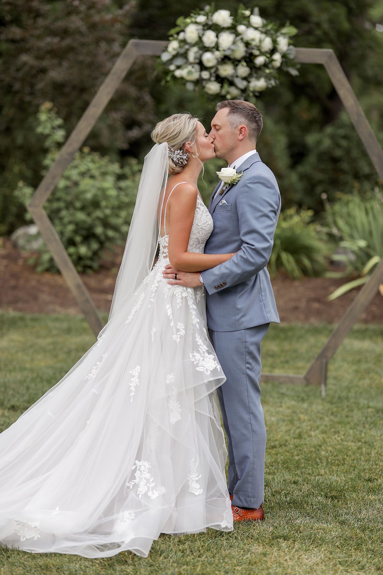 Elegant outdoor wedding portraits featuring flowing white gown and floral details in a garden setting.