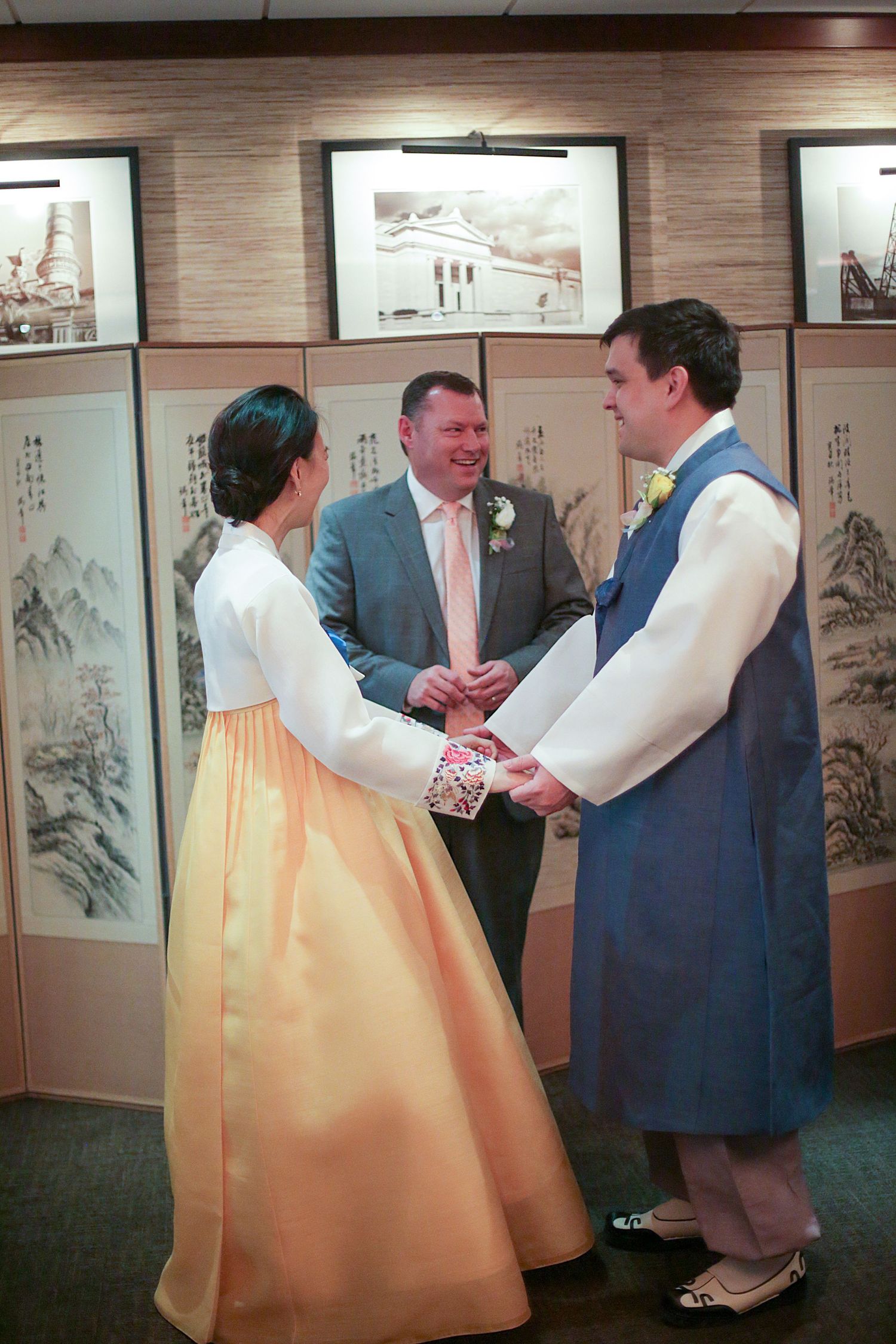 A traditional Korean wedding ceremony takes place in front of decorative scroll paintings with the couple in hanbok attire.