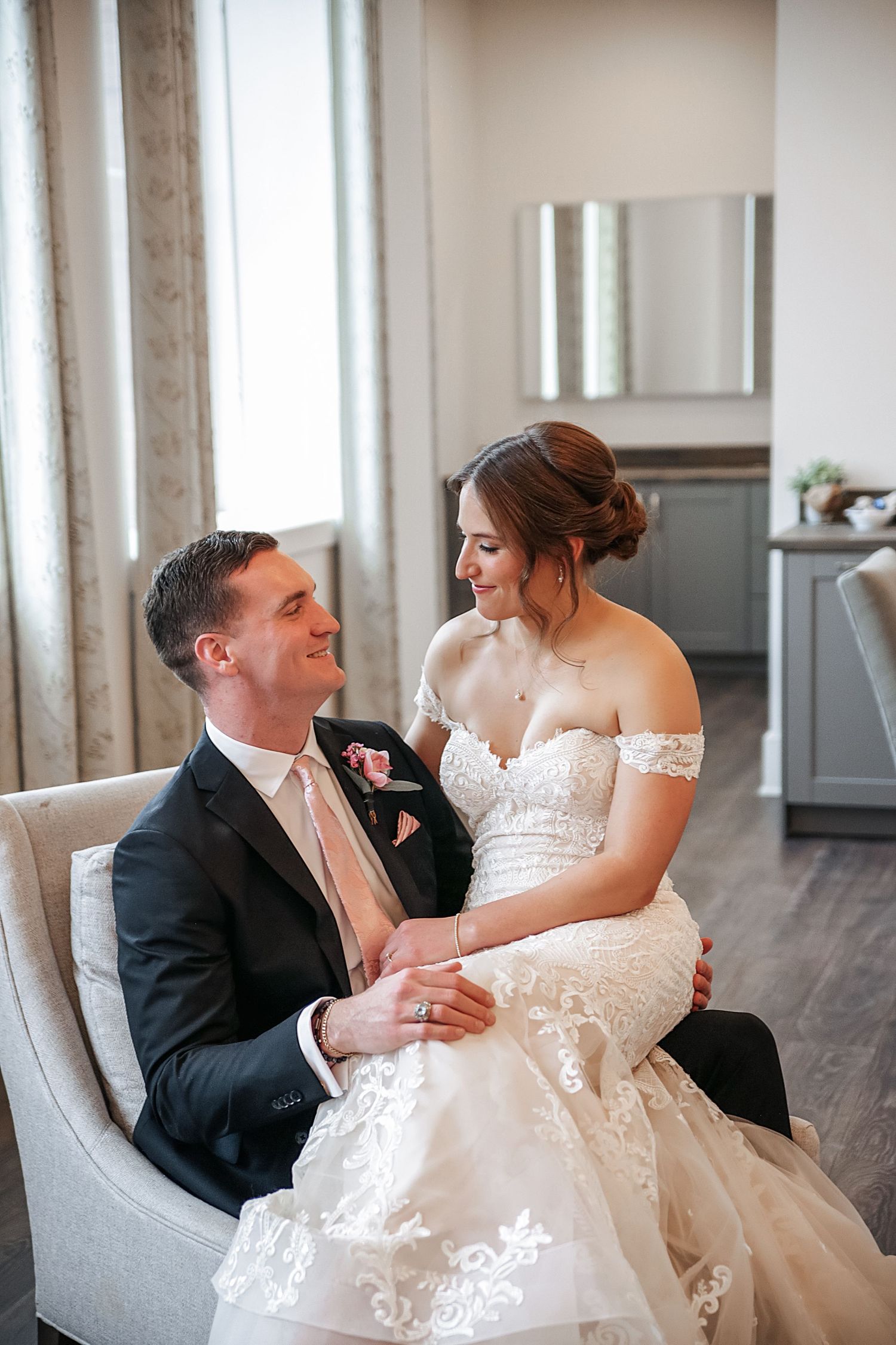 Newlywed couple shares intimate moments while sitting together in elegant white chairs at their wedding venue.