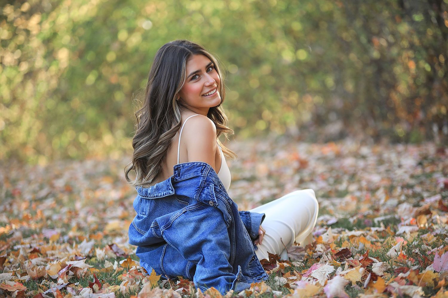 A woman in a blue dress lies gracefully among autumn leaves during an outdoor photo session.