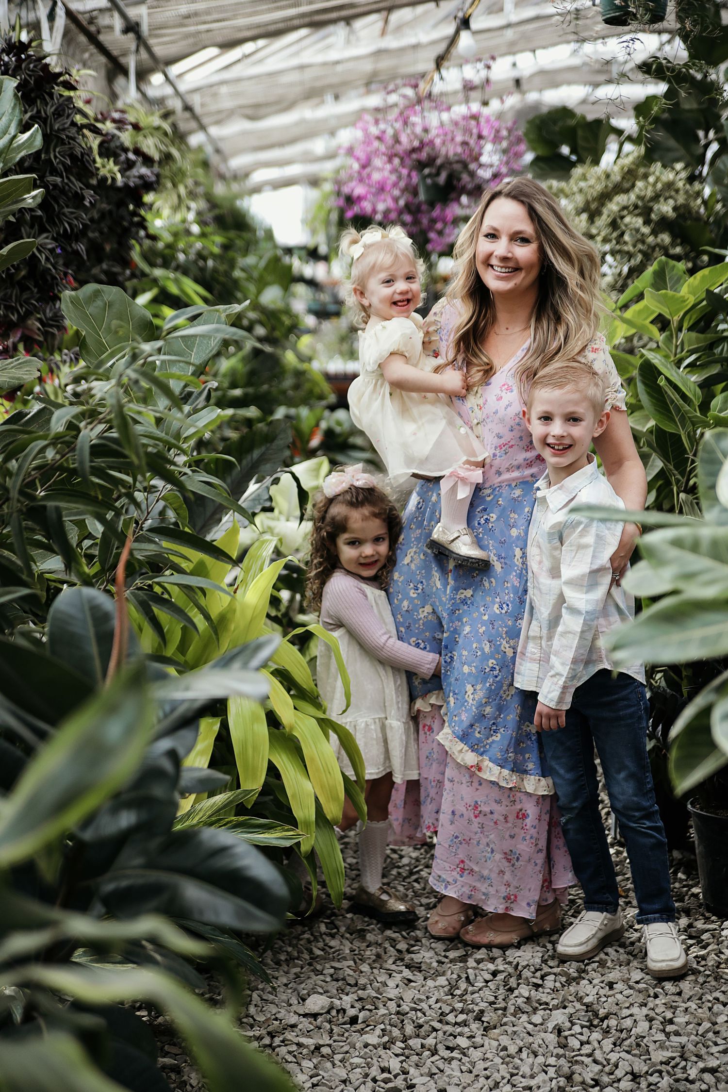 A family explores together inside a lush greenhouse filled with tropical plants and blooming orchids.