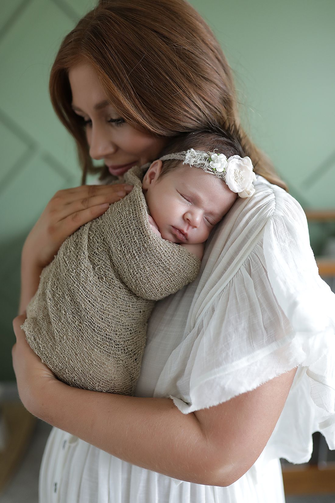 Tender moment between parent and baby in white dress against green wall. Newborn photographer Medina, Ohio.