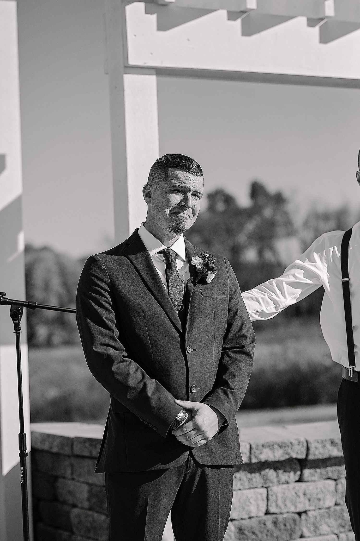 A person in a black suit stands at attention during an outdoor wedding ceremony.