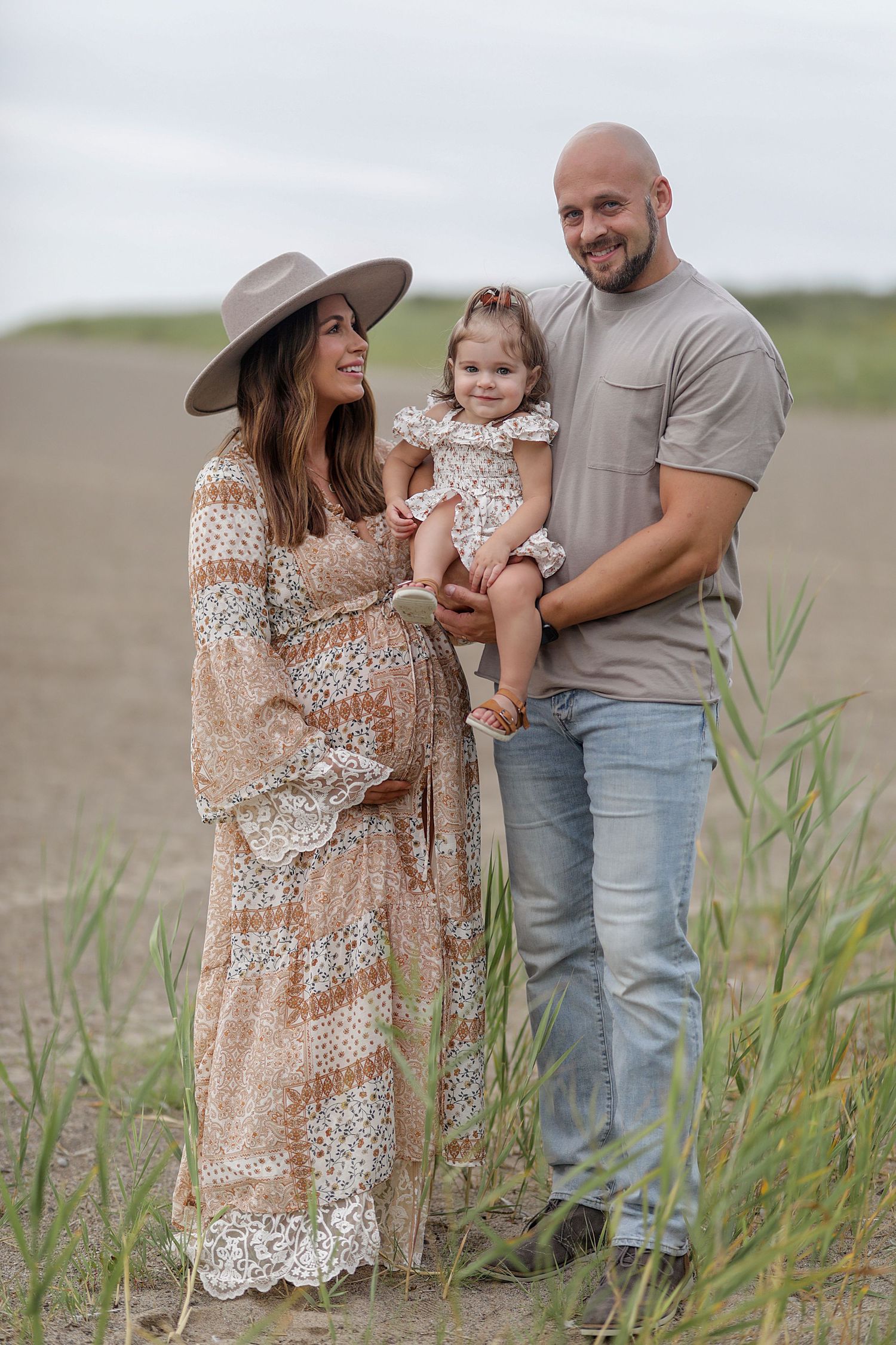 Family wearing coordinated neutral outfits poses together in tall grass during a casual outdoor photo session.