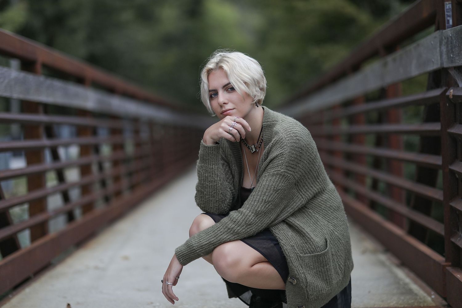Someone sits contemplatively on a wooden bridge walkway with trees and nature in the background.