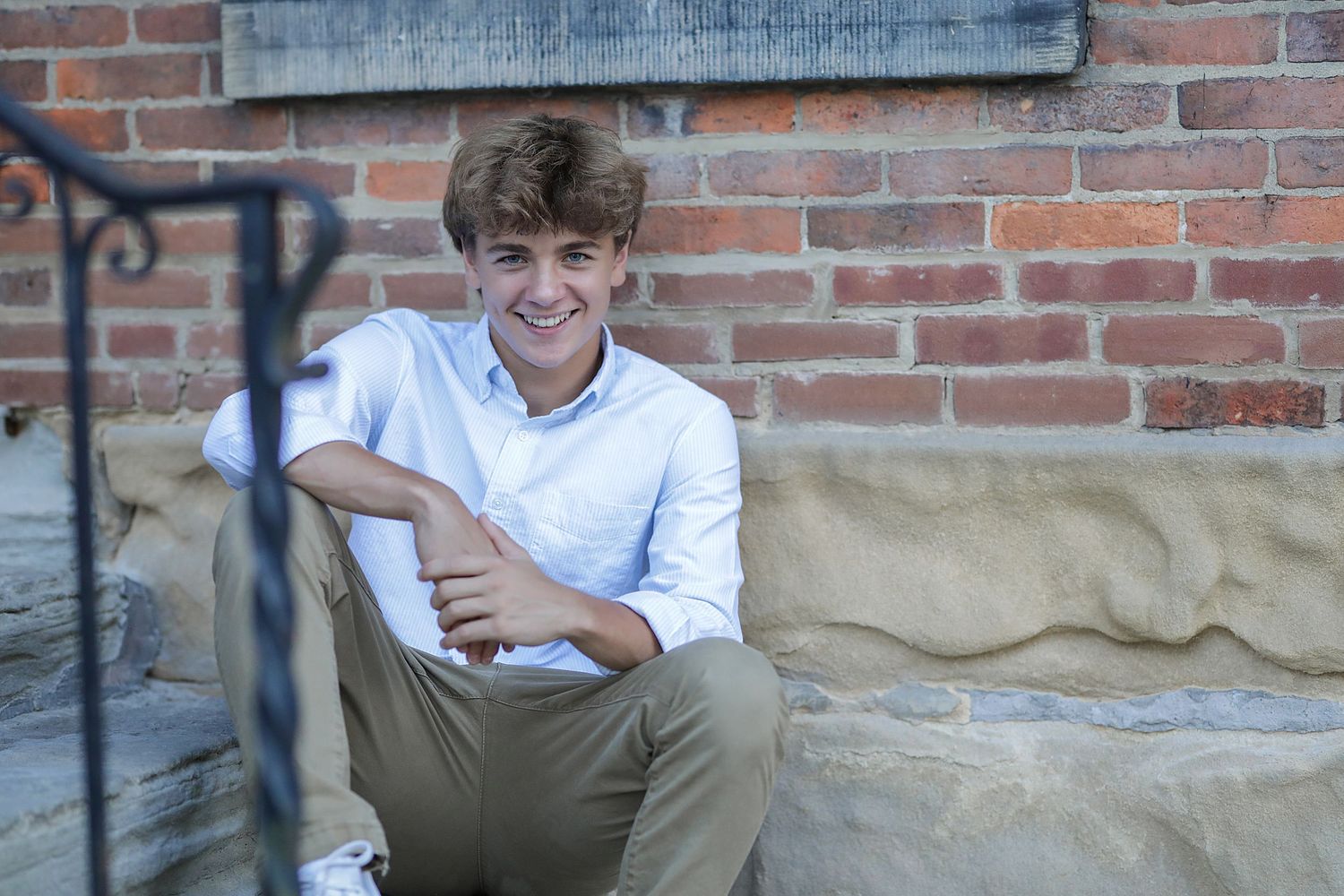 Someone sits smiling in white button-up shirt against brick wall background with blurred frames visible.