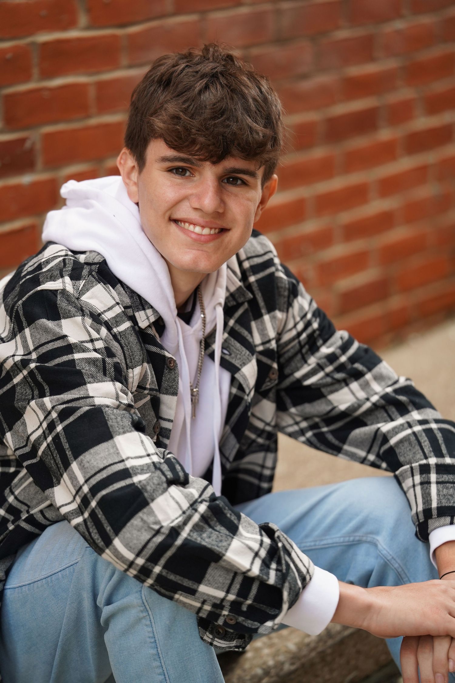 Portrait of a person wearing a black and white plaid flannel shirt over a white hoodie against a brick wall.