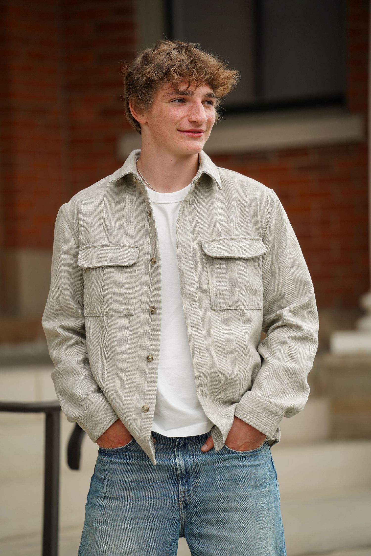 Casual outdoor portrait showing someone wearing a beige utility jacket over a white t-shirt with blue jeans.