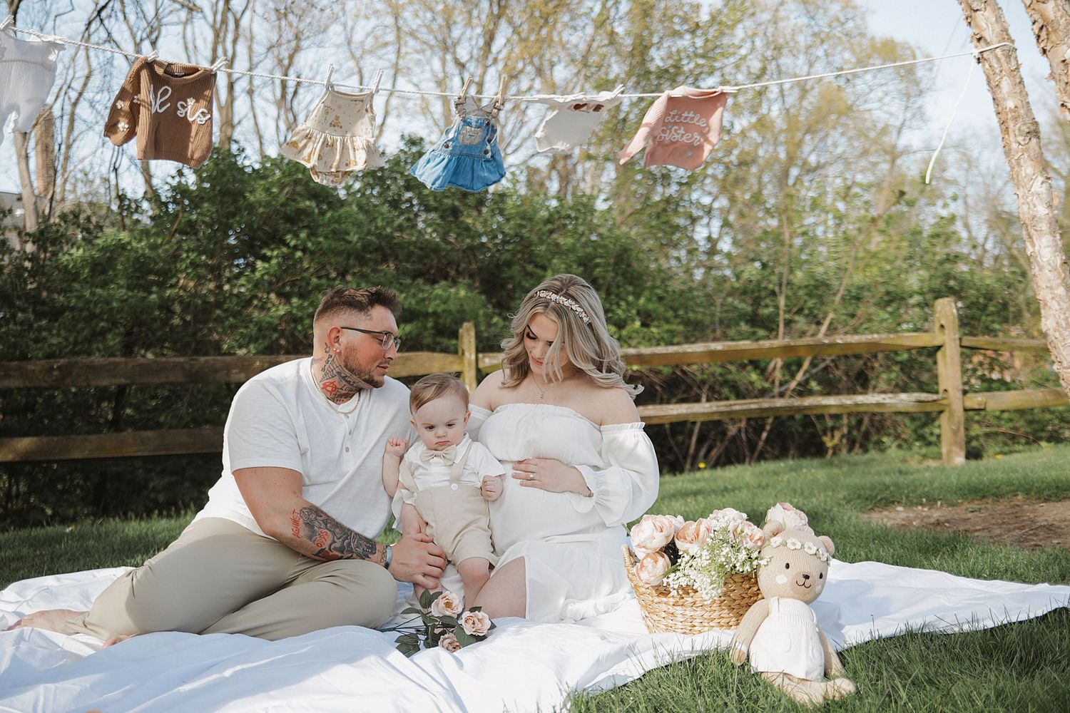 A couple relaxes together on a white blanket laid out on the grass near birch trees on a sunny day.