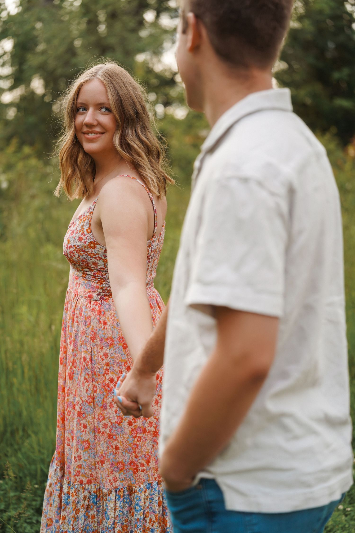 A couple shares a romantic moment outdoors as they pose together in a grassy field during golden hour.