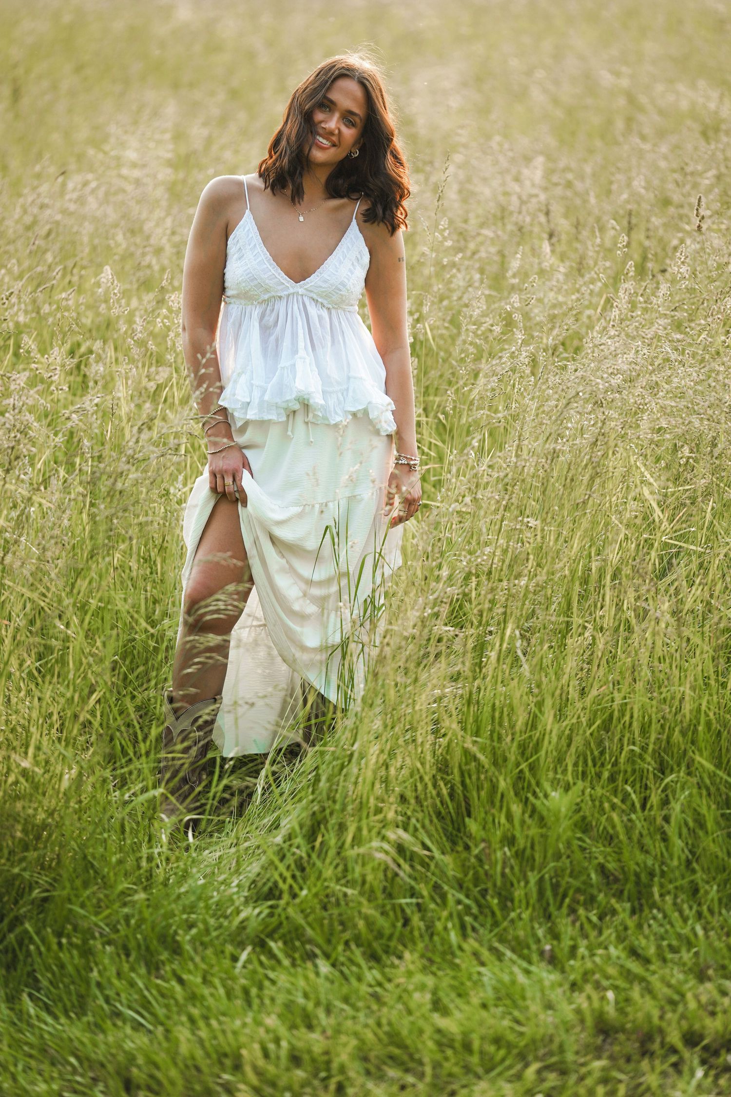Ethereal golden-hour photography of a figure in white moving gracefully through wild grass in a natural field setting.
