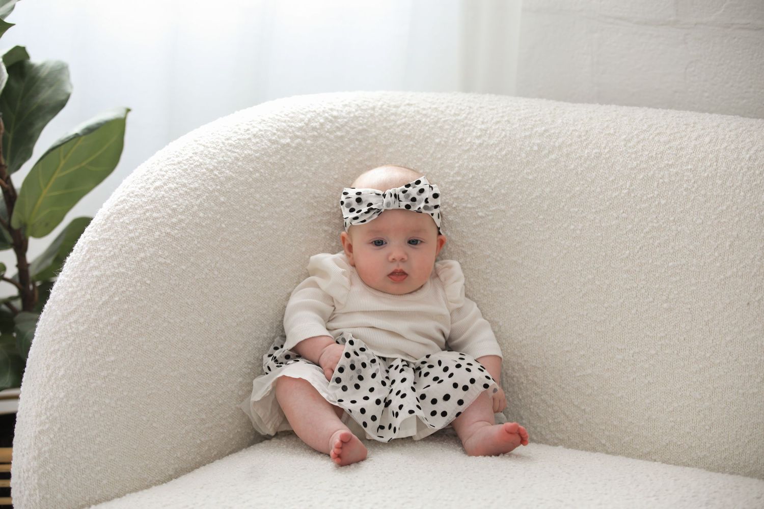 A baby wearing a white and black polka dot outfit lies on a white couch in a series of poses.