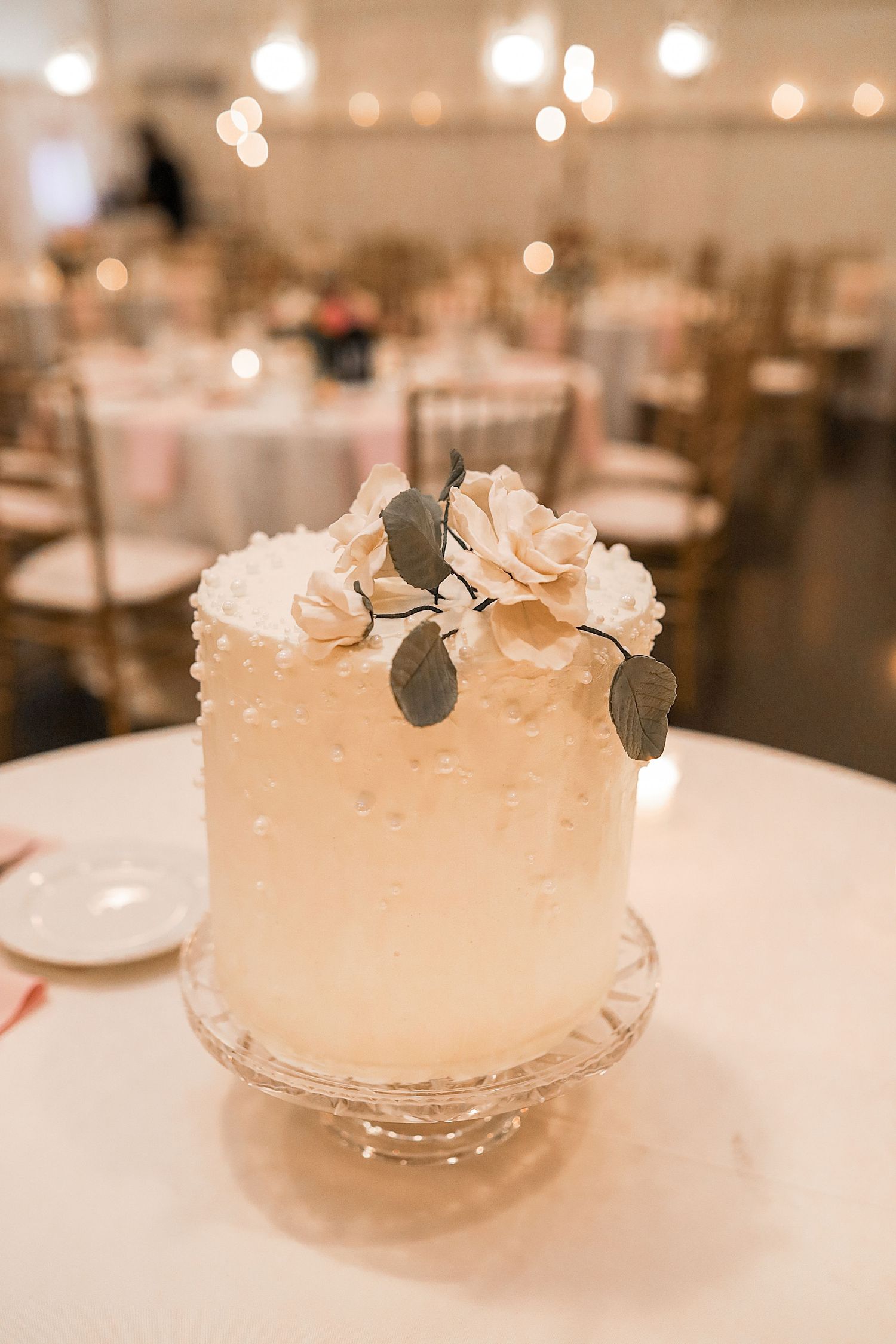 A decorative white wedding cake with delicate floral details and soft lighting in an elegant reception setting.