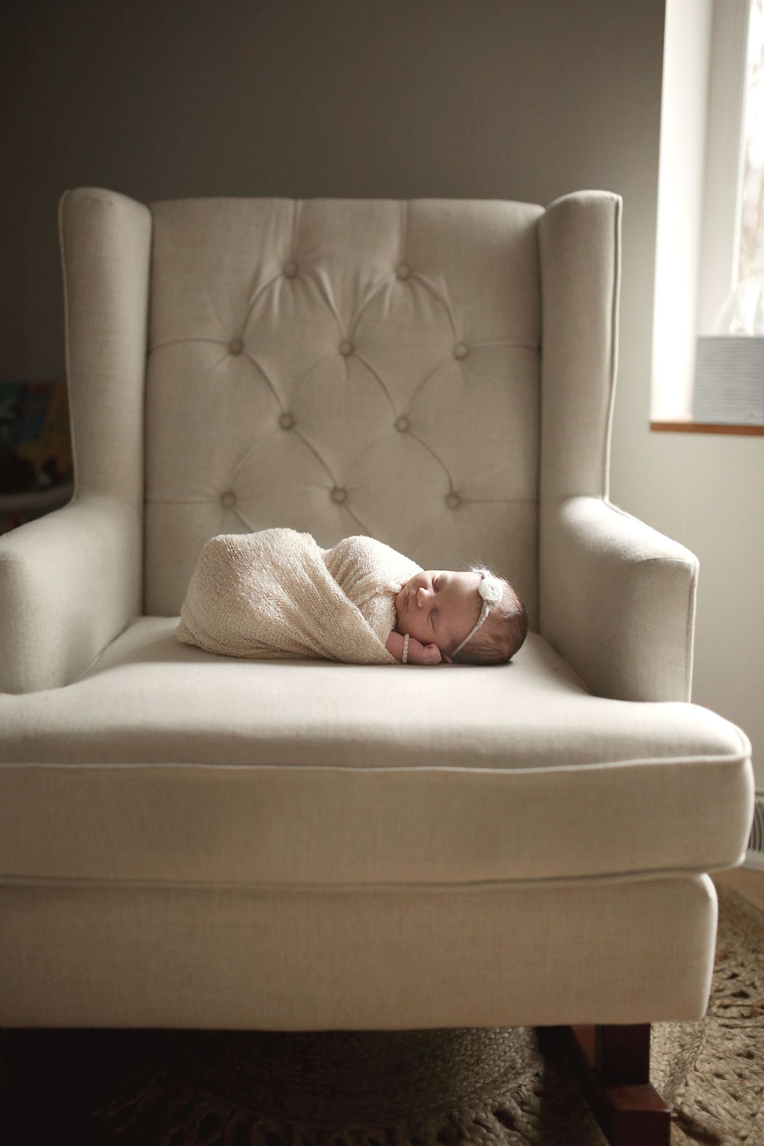 Newborn baby wrapped in white swaddle sleeping peacefully in tufted wingback chair. Newborn photographer Medina, Ohio.