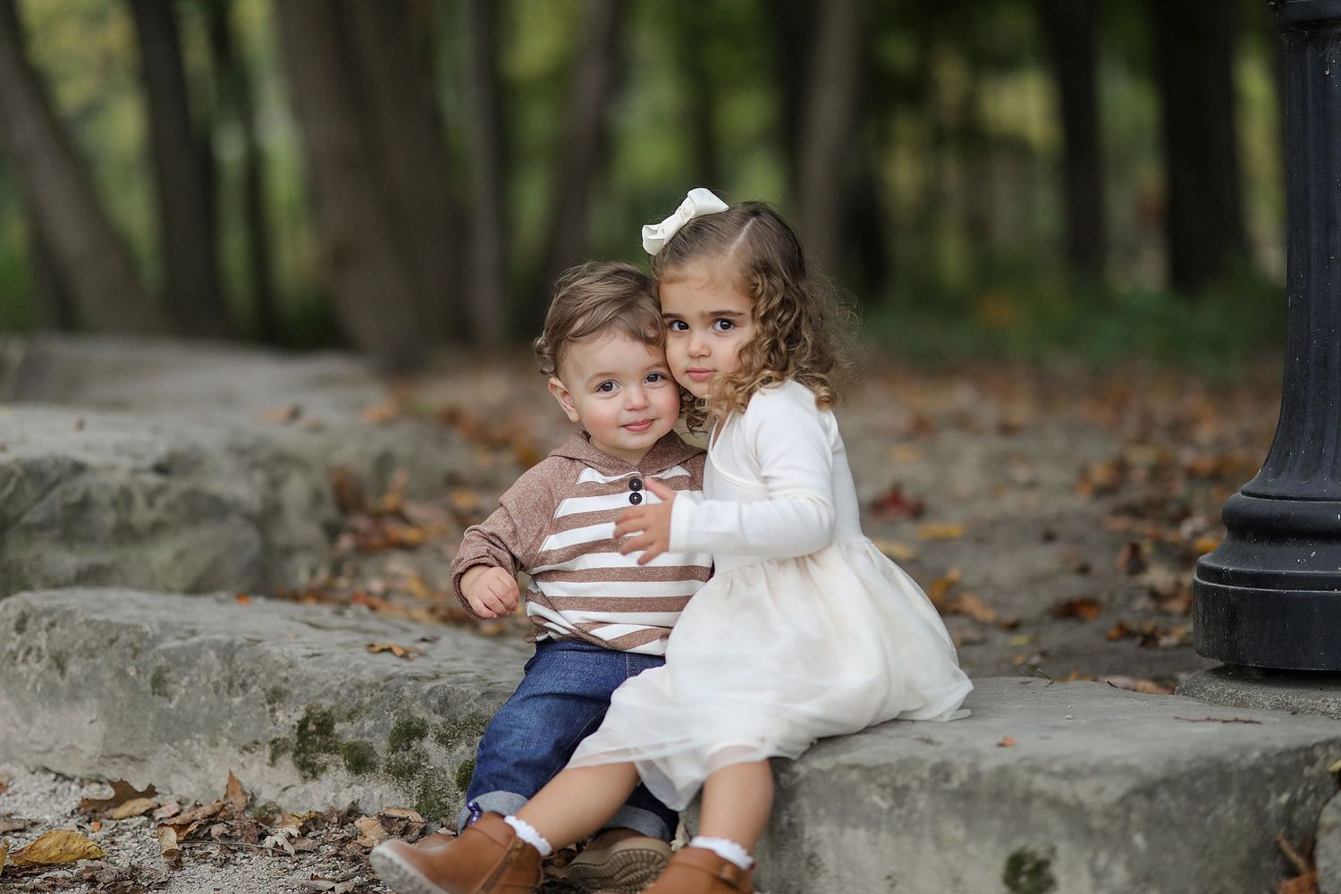 Two young children sitting close together on stone steps surrounded by autumn leaves.  Family Photography in Strongsville Ohio