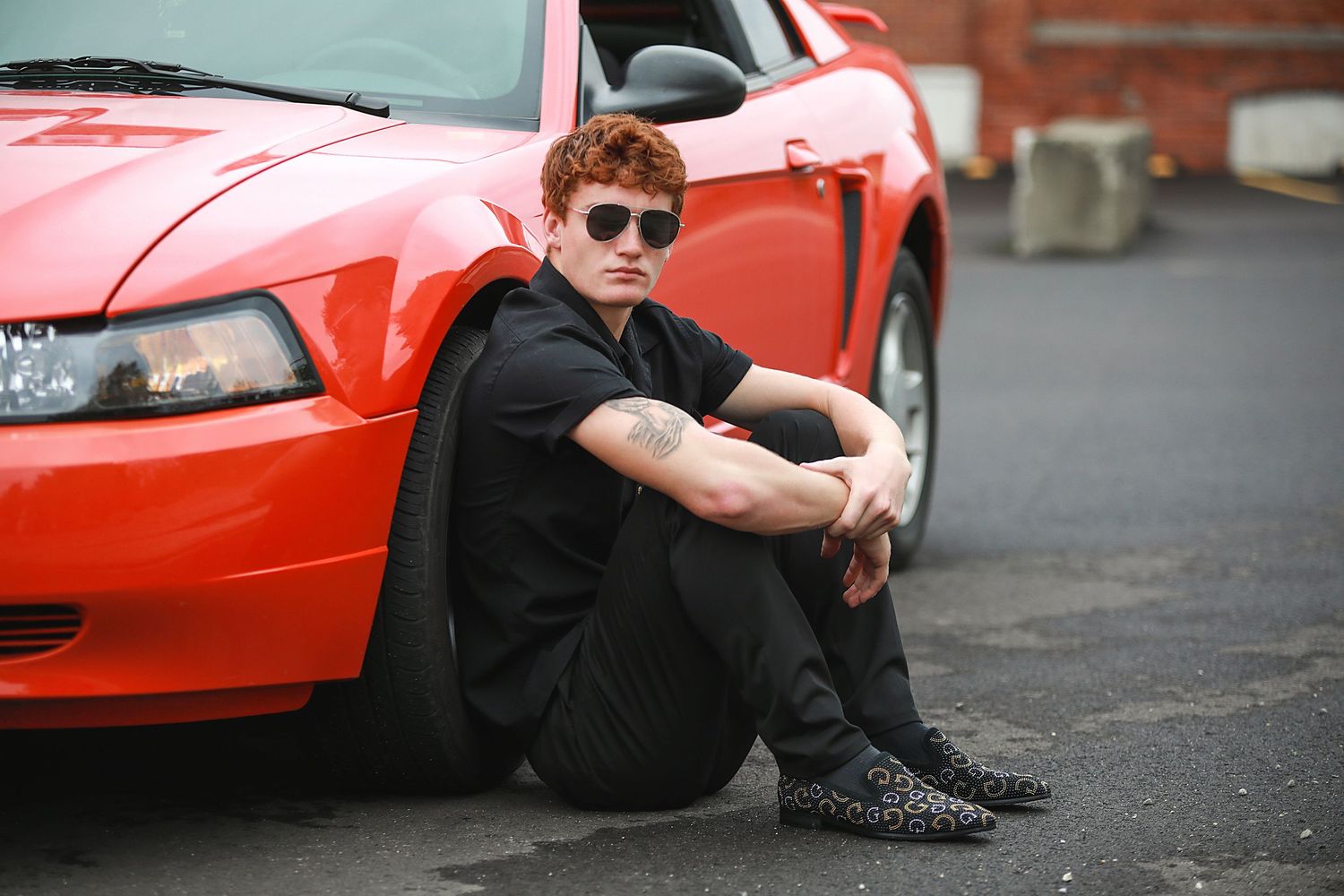 Senior Portraits Wadsworth Ohio. A person in black clothing and sunglasses sits next to a bright red Mustang car.