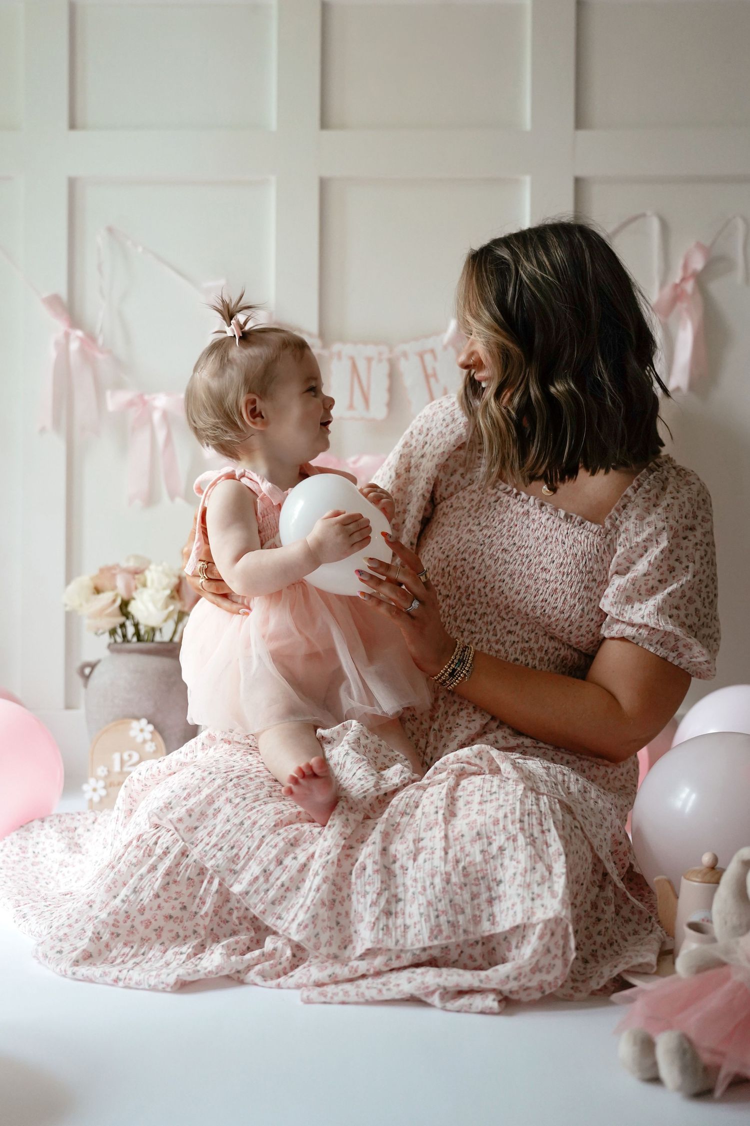A tender moment during a pink-themed party with polka dot dresses, balloons and decorative wall panels.