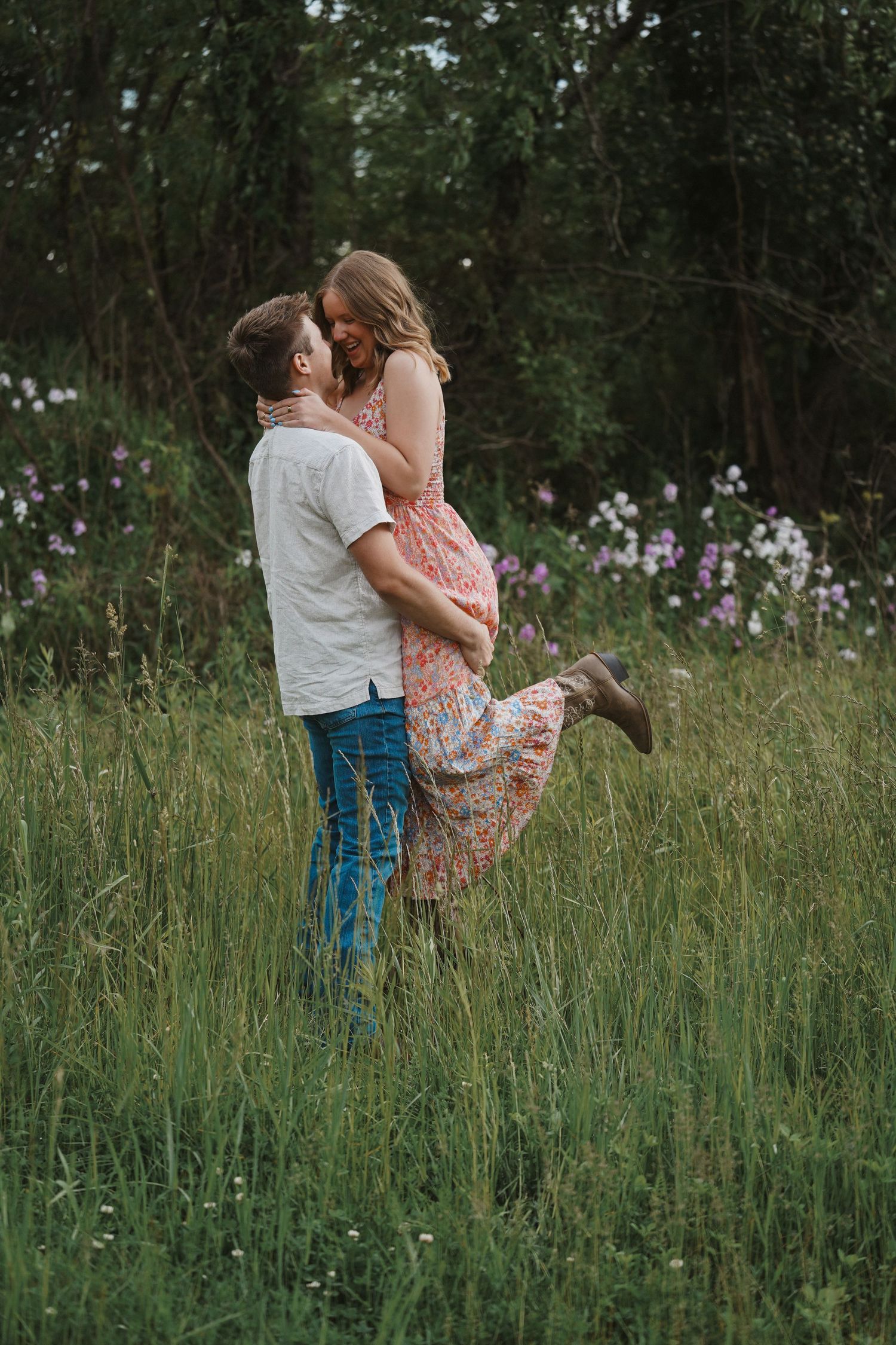 A couple embraces in a field of tall grass and wildflowers on a cloudy summer day.