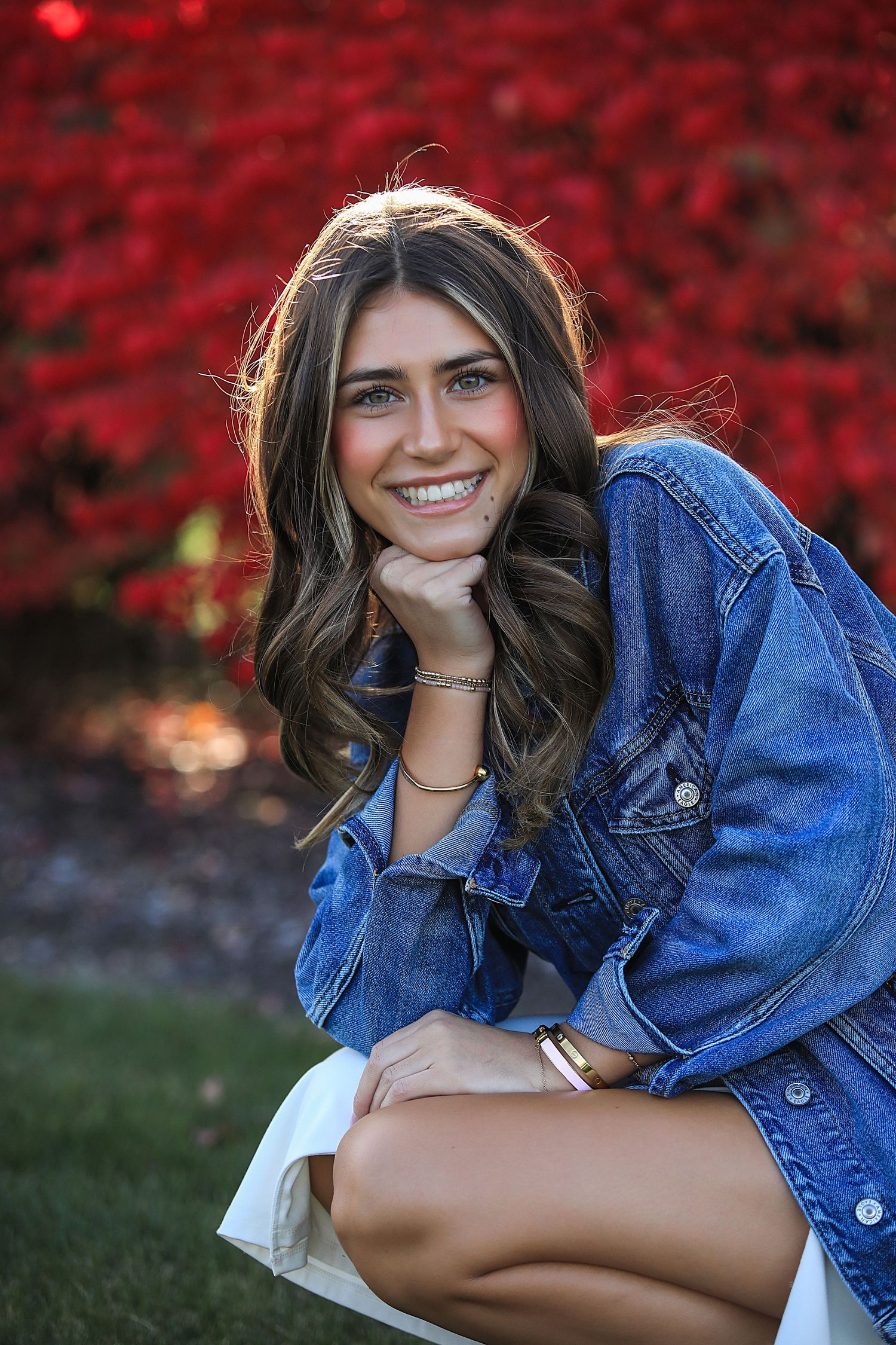 Portrait with denim jacket against vibrant red autumn foliage background.