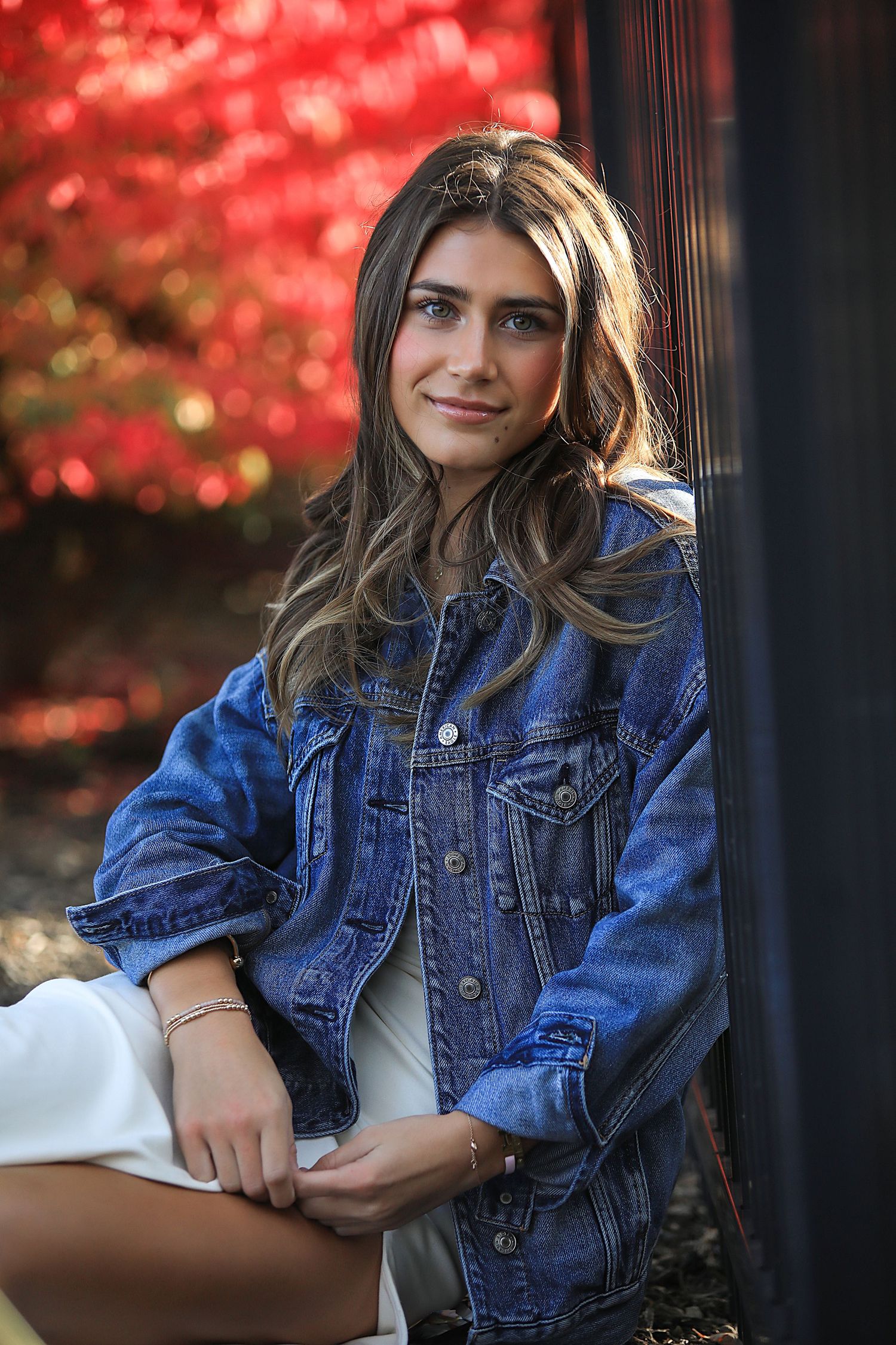 Portrait photo with autumn red foliage background showing person in denim jacket with flowing highlighted hair.