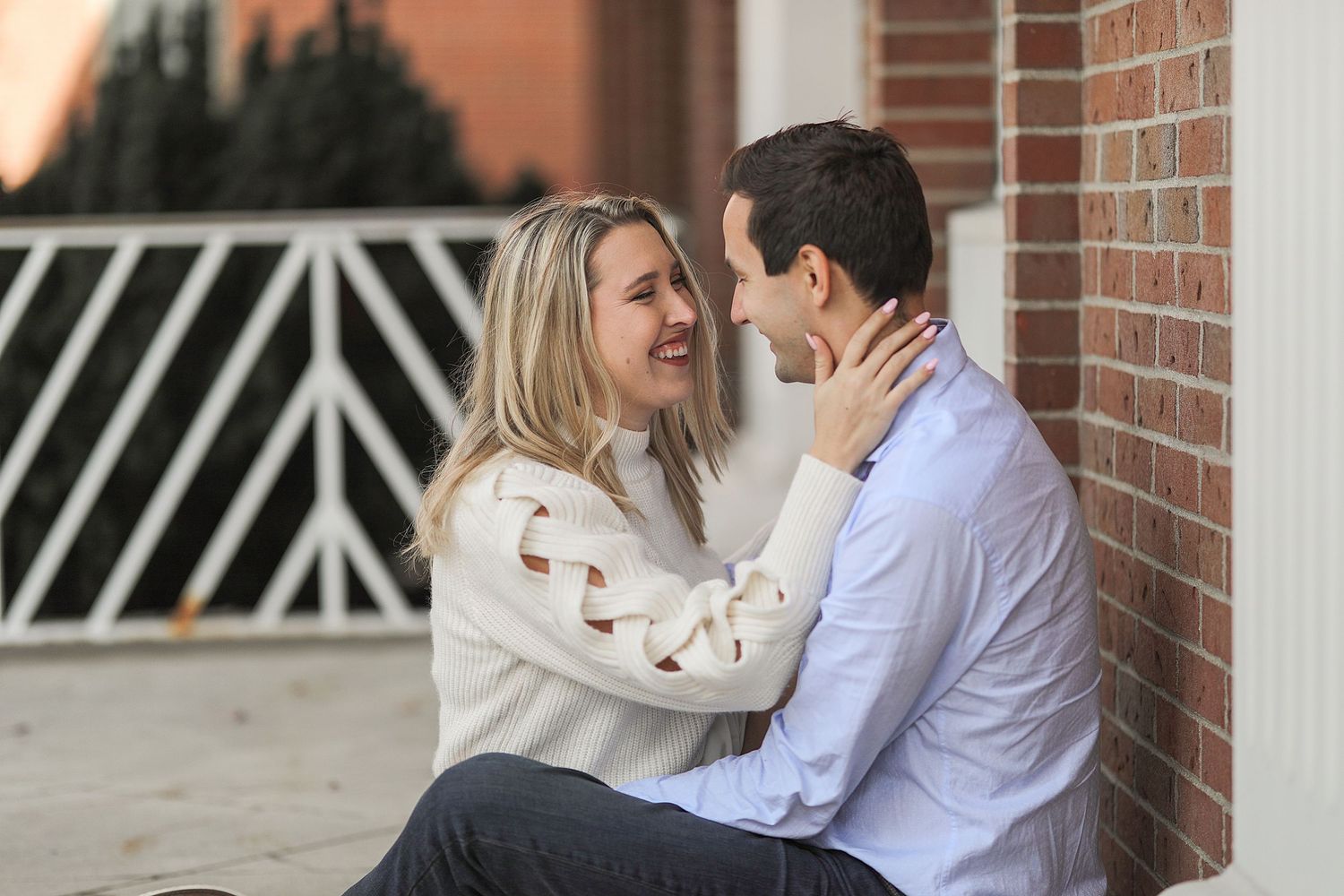 Romantic couple in white sweaters share an intimate moment against a brick wall at sunset.