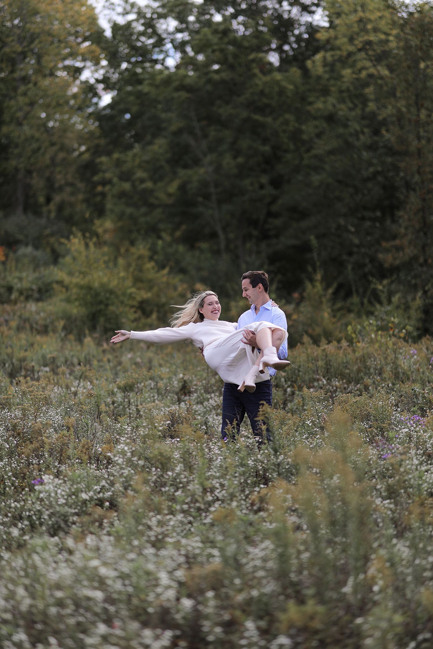 A couple dances in a wildflower meadow surrounded by trees on a romantic afternoon.