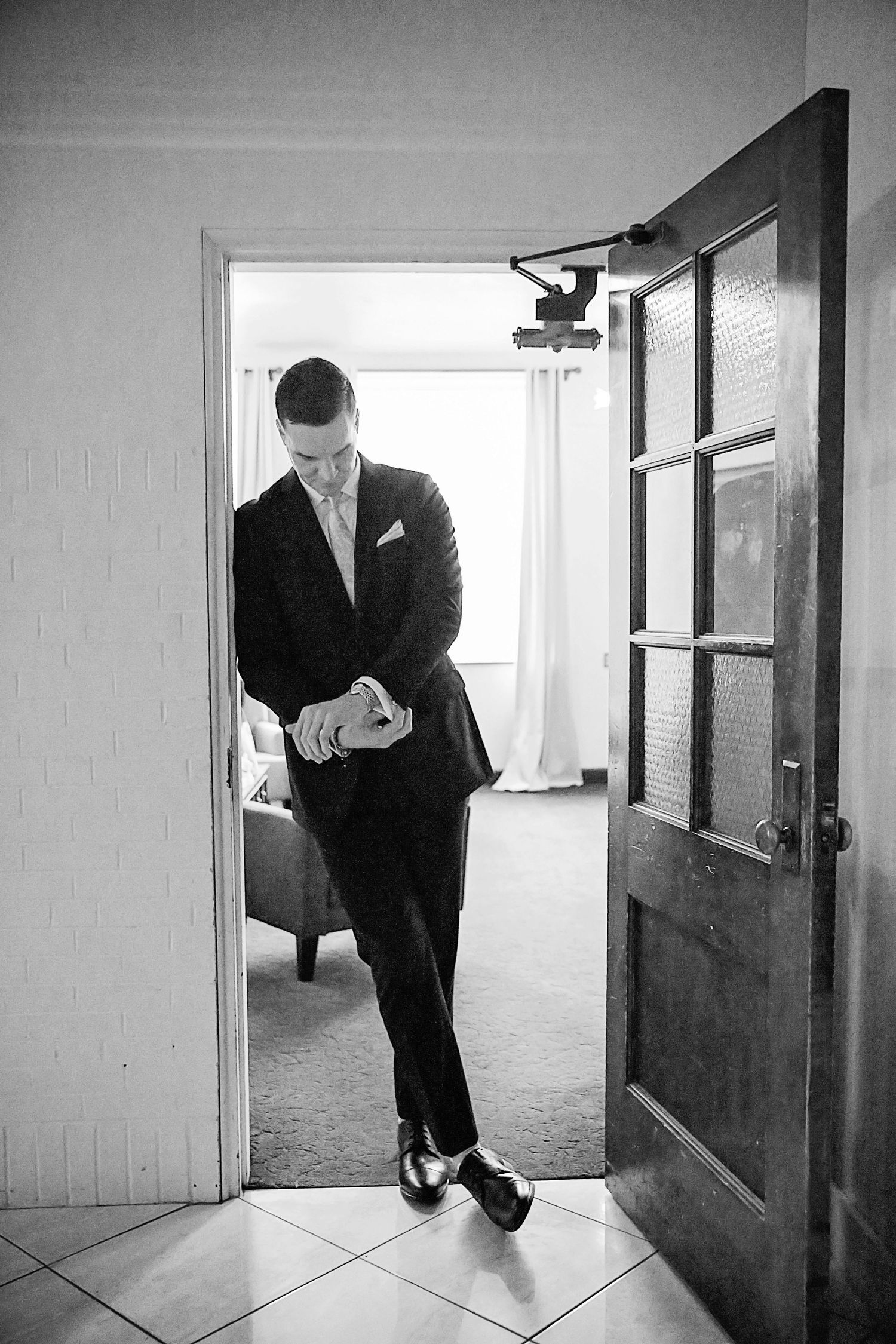 A series of black and white photos showing a person in a suit peeking through doorways in an empty hallway.