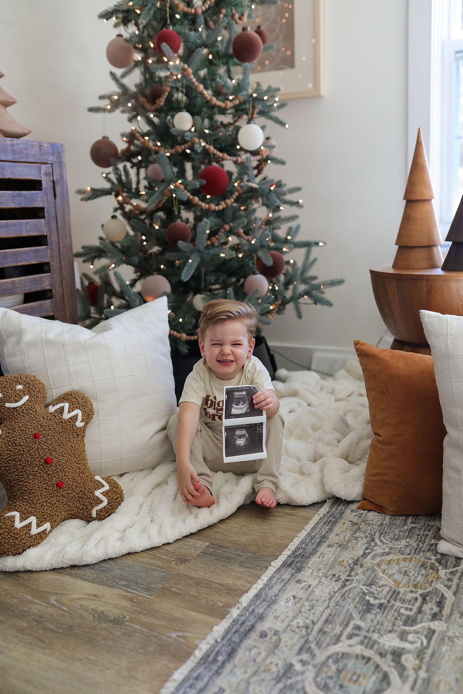 A decorated Christmas tree and cozy holiday scene with gingerbread pillows on the floor and wooden accents.