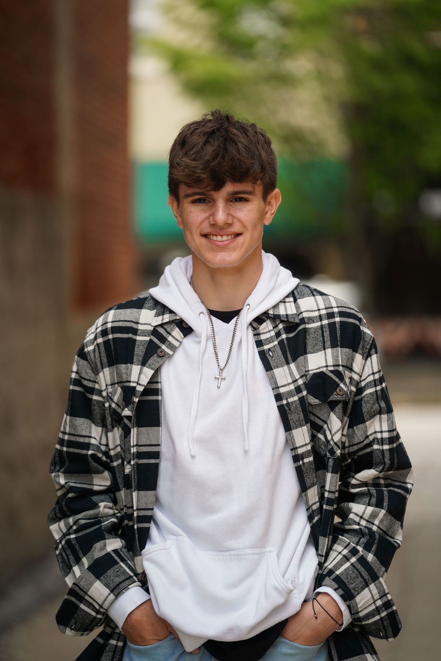 A person poses in a casual outfit featuring a white hoodie and black and white plaid flannel shirt.