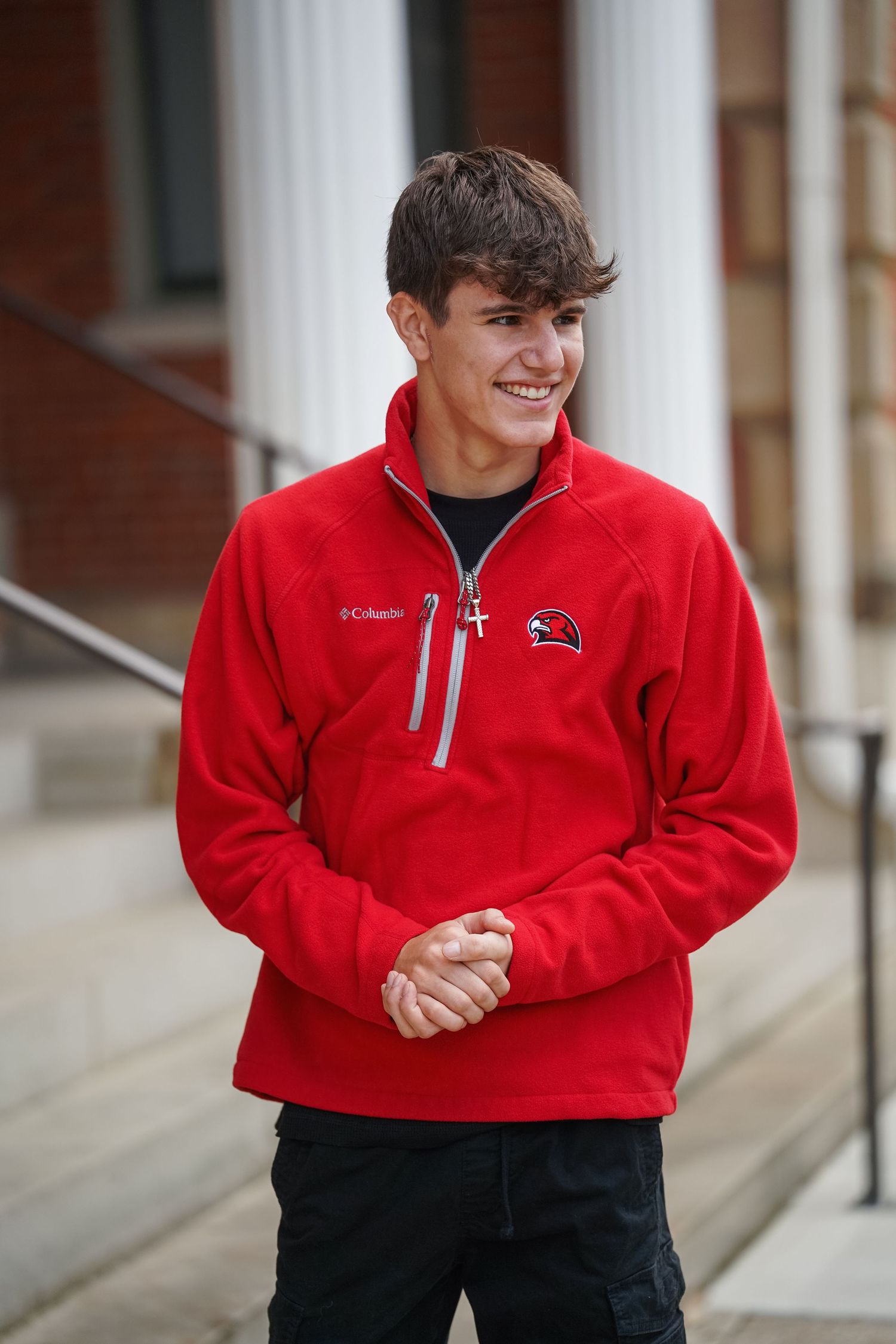 Student wearing a bright red Columbia fleece pullover with black pants smiles while standing on campus steps.
